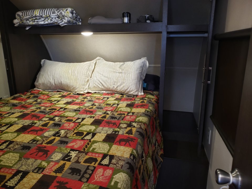 Cozy RV rental bedroom featuring a patterned quilt, comfy pillows, overhead storage, and an empty wardrobe.. Forest River Cruise Lite 2018