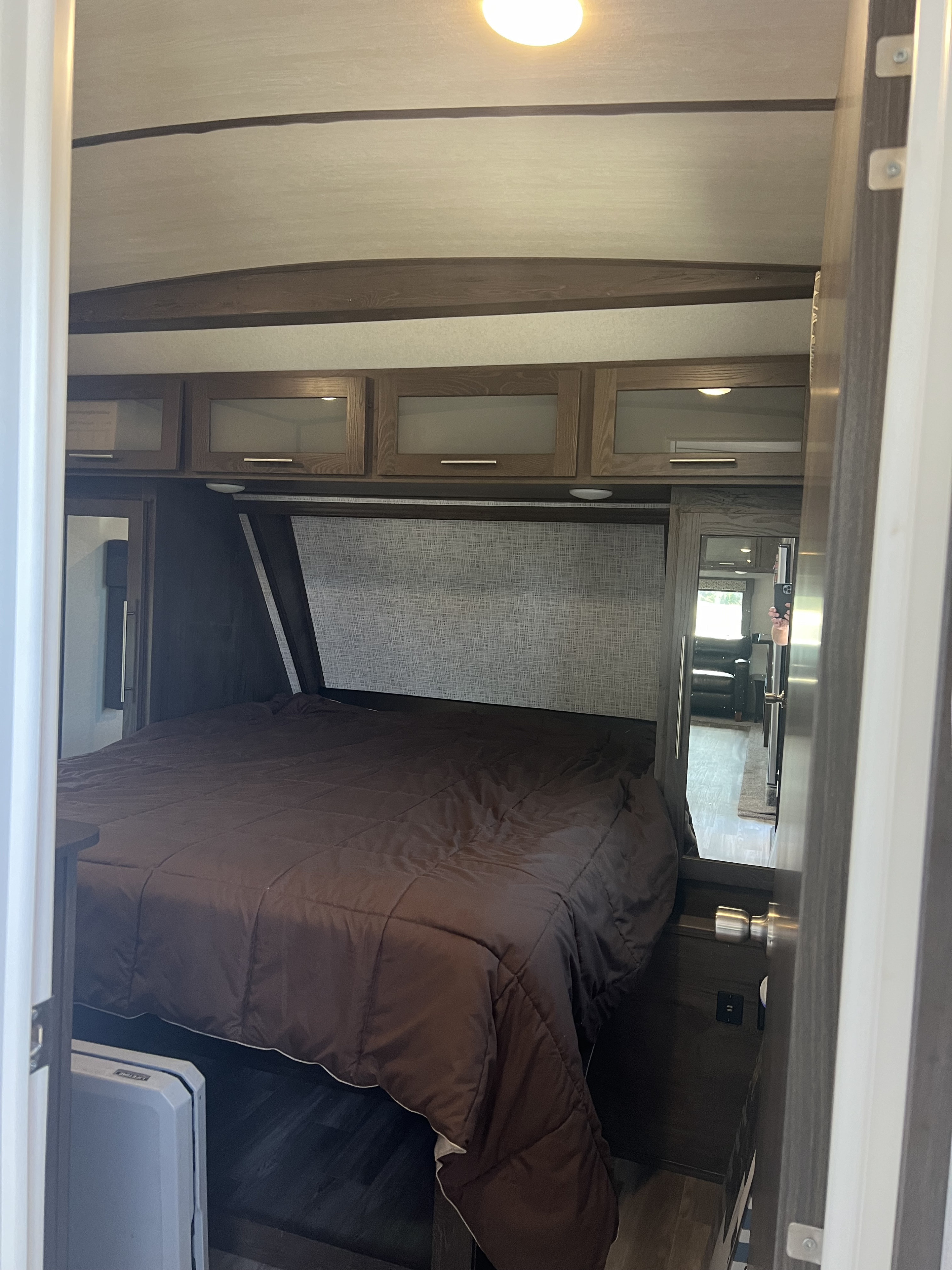 This RV rental bedroom features a comfy bed with a brown comforter, overhead storage, and a mirror showing the living area.. Forest River Salem Hemisphere GLX 2019