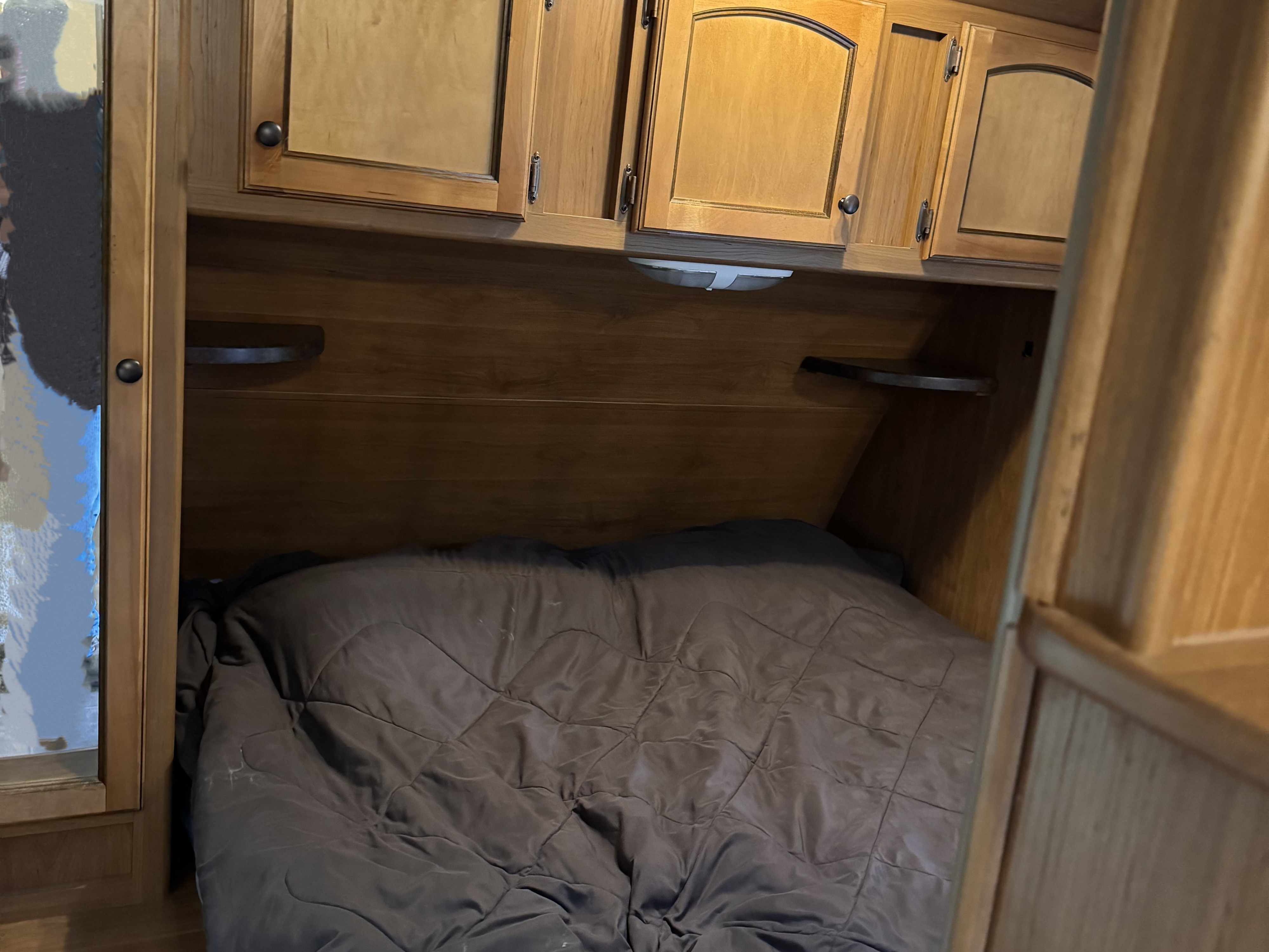 Cozy RV rental bedroom with a comfortable bed, wooden overhead storage cabinets, and side shelves for essentials.. Crossroads Sunset Trail 2014