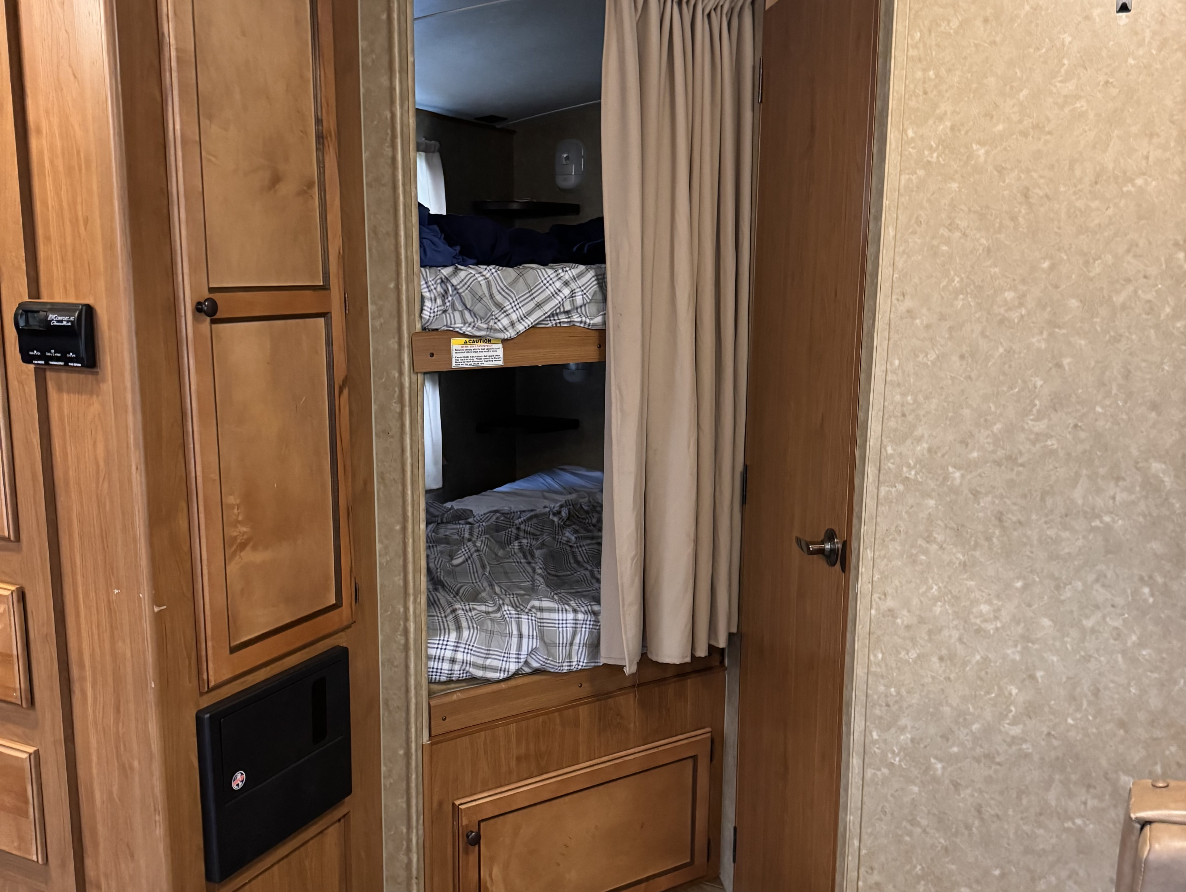 Interior of an RV rental: bunk beds with plaid bedding, wood cabinetry, and a climate control panel.. Crossroads Sunset Trail 2014