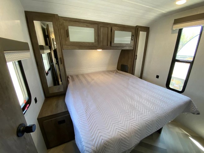 Comfortable RV rental bedroom with a queen bed, overhead cabinets, and windows for your next adventure.. Forest River Wildwood 2021