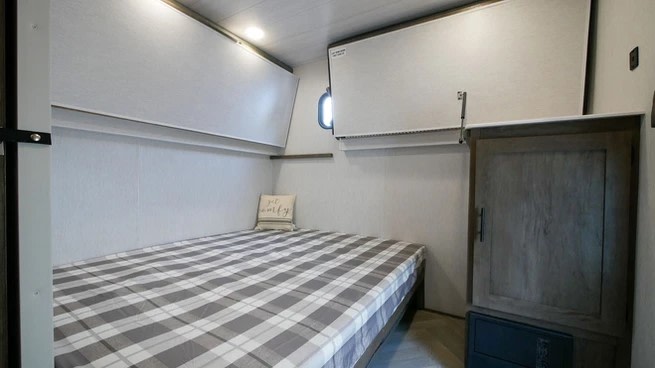 Inside an RV rental: a bunk bed with plaid covers, overhead storage, and a small window, offering a cozy sleeping space.. Forest River Wildwood 2021