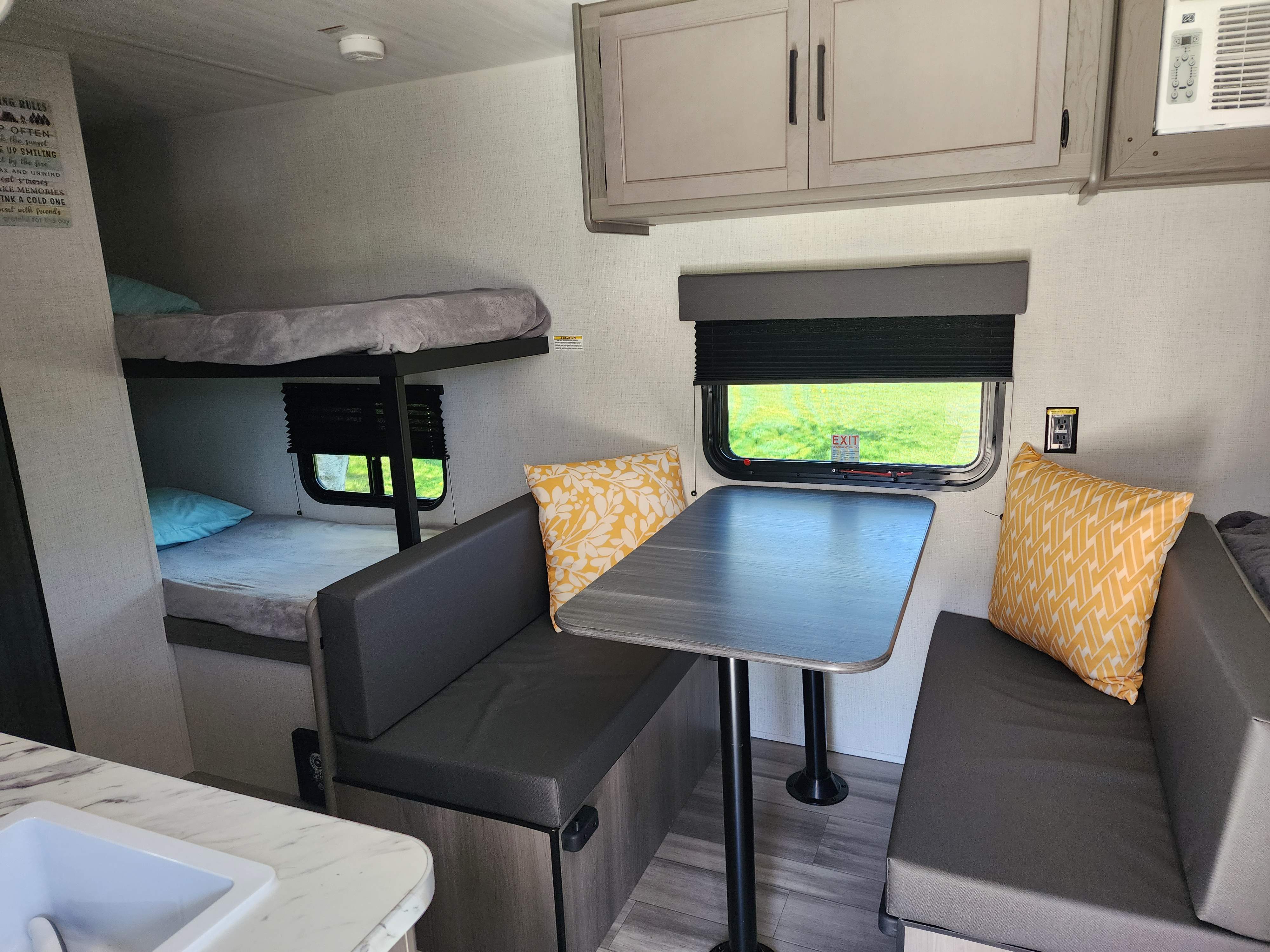 Spacious RV rental interior featuring bunk beds, a dinette table, and overhead cabinets, perfect for family trips.. Keystone RV Hideout 175BH 2024