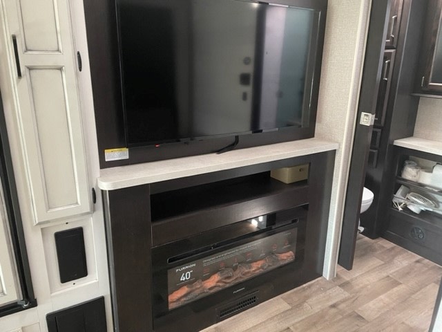 Modern RV rental interior with a wall-mounted TV, electric fireplace, and built-in storage. Bathroom visible through doorway.. Entegra Coach Odyssey 2021