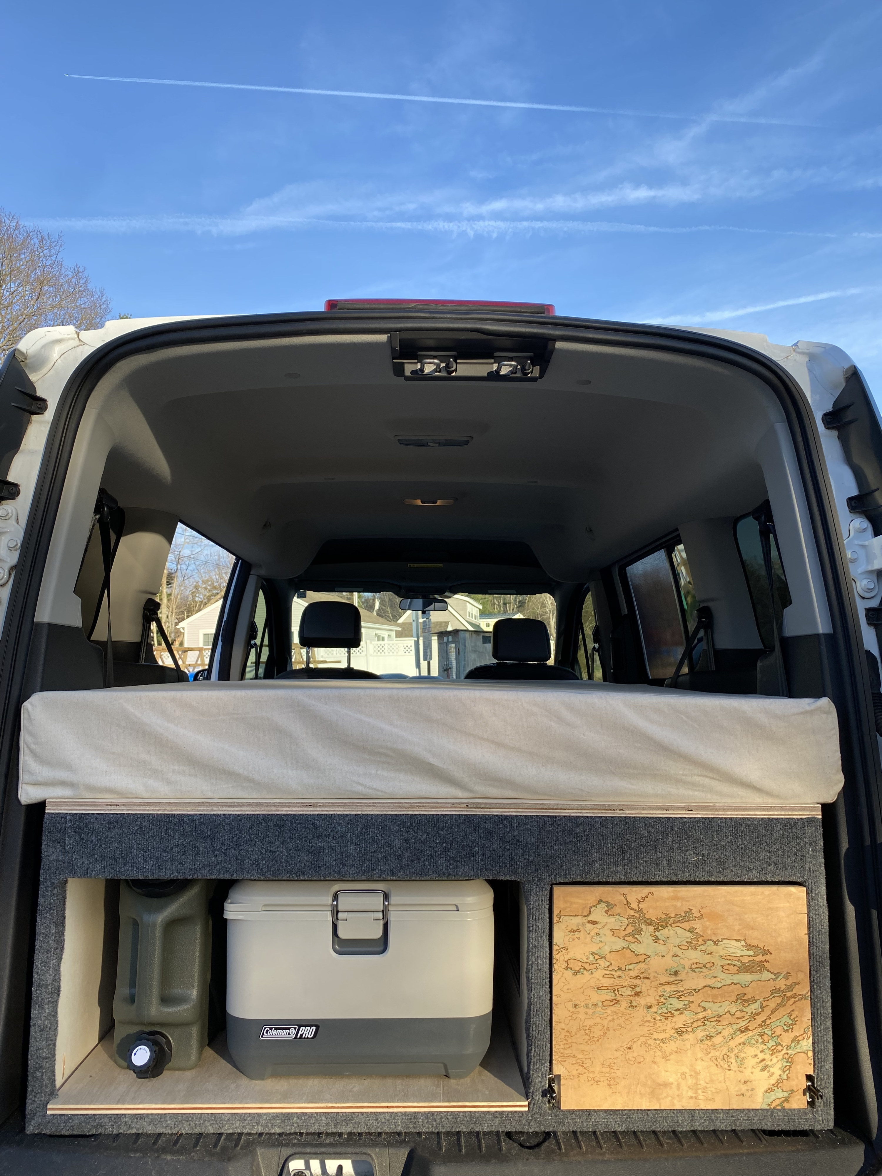 Rear view of a camper van conversion, showing a mattress, water jug, Coleman cooler, and map panel. Ideal for an RV rental or road trip.. Ford Transit Connect 2017