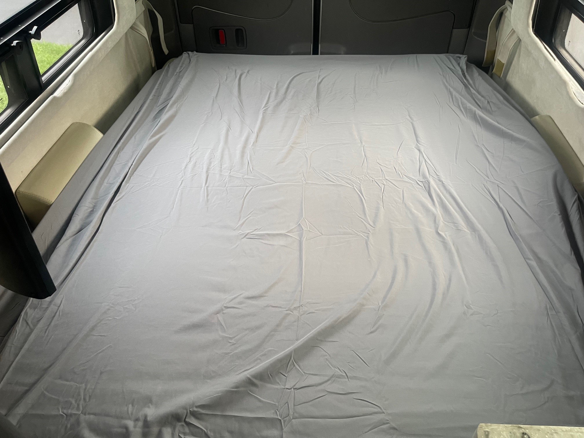 Inside an RV rental: a neatly made grey bed fills the spacious rear area, with windows on the sides, ready for travel.. Airstream Interstate 2014
