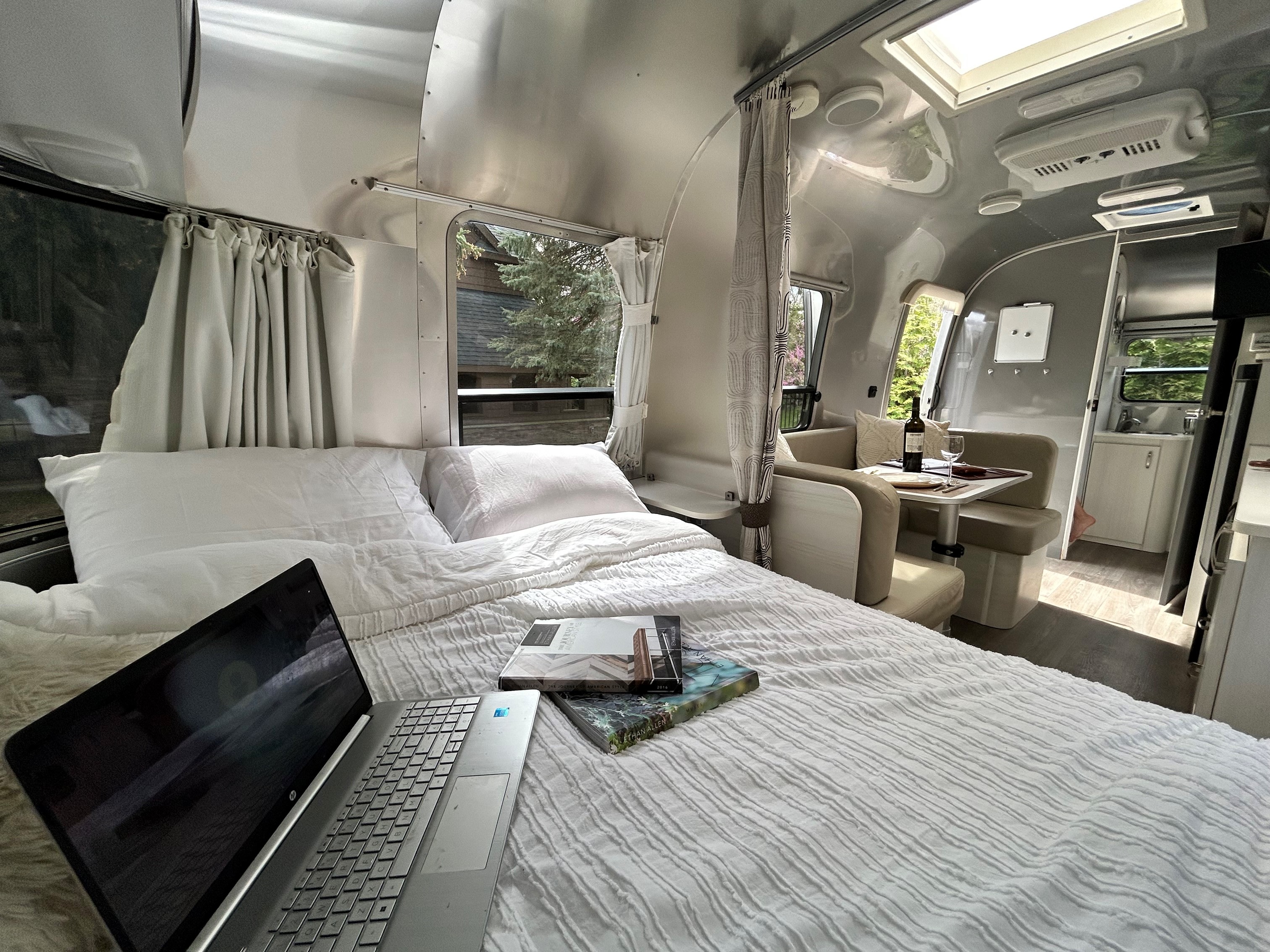 Inside a chic Airstream rv rental showing a bright bedroom with a laptop, cozy dining area, and compact kitchen.. Airstream Sport 2018