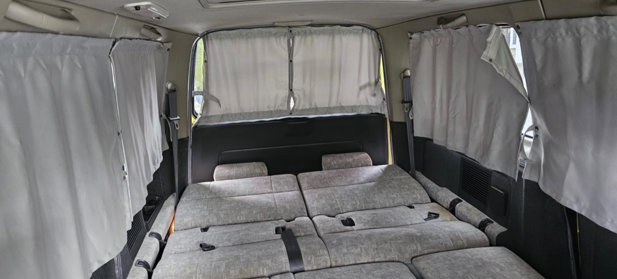 Interior of an RV rental camper van with seats folded into a bed and privacy curtains drawn, perfect for travel.. Other Other 2000