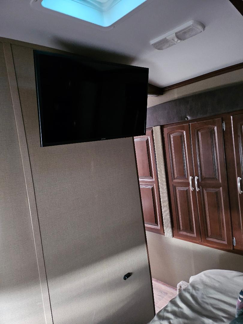 Inside an RV rental: a bedroom with wall-mounted TV, wood cabinets, skylight, and compact design.. Keystone Outback 2016