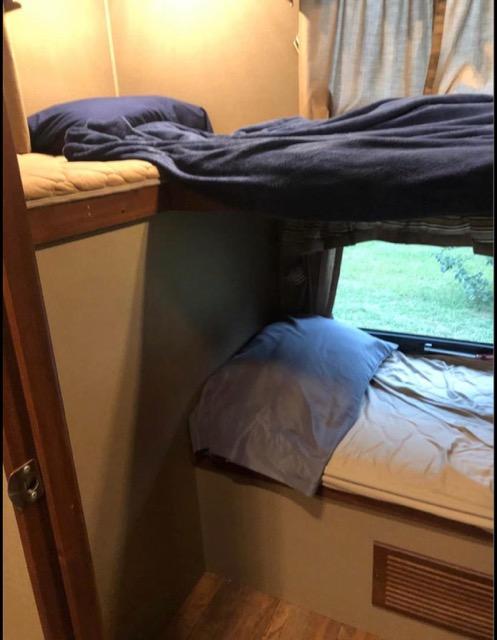 Cozy RV rental interior features stacked bunk beds with blue bedding. The lower bunk has a window revealing green scenery.. Keystone Outback 2016