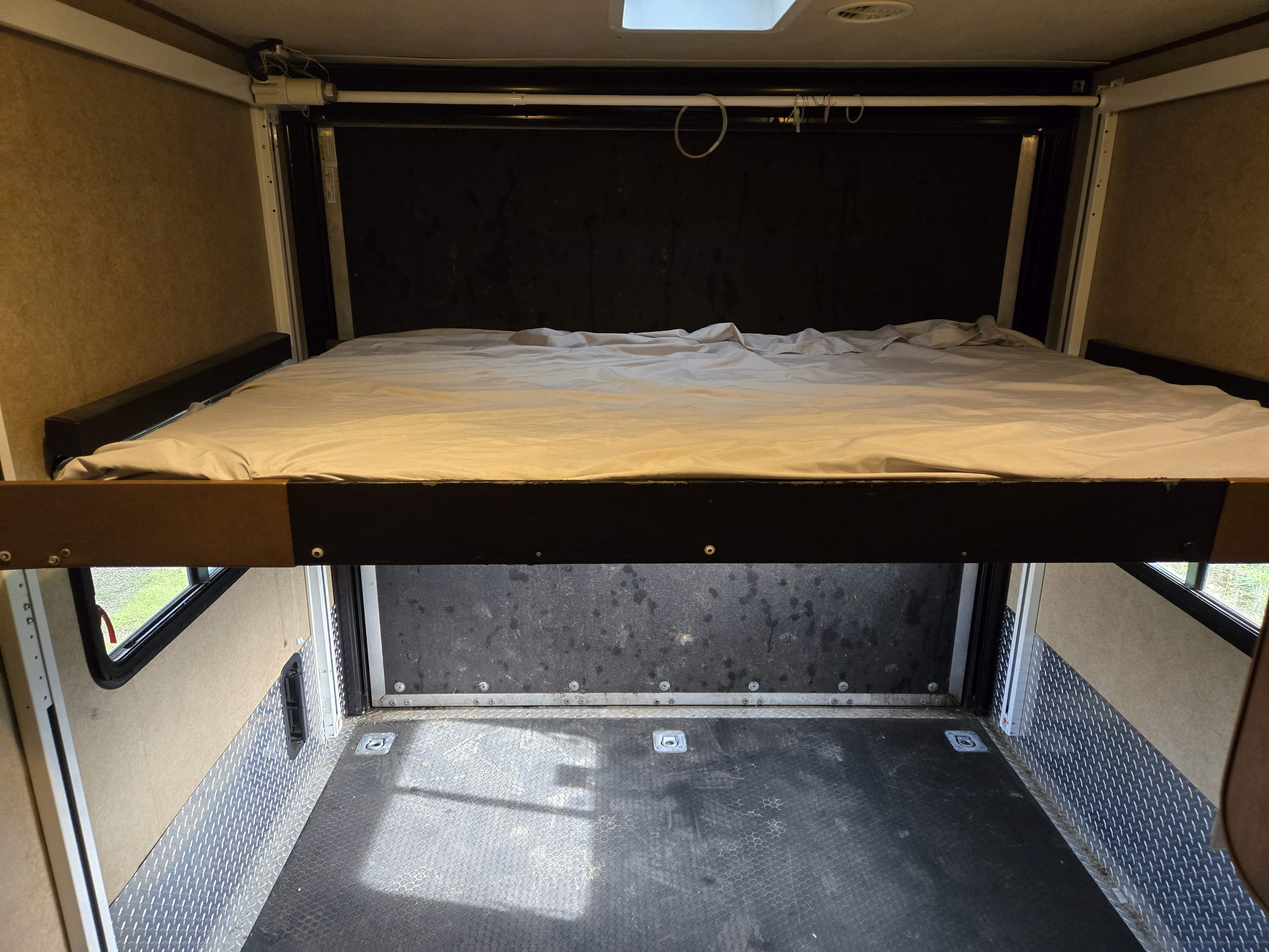 Toy hauler RV rental interior: A power-lift bed is raised, revealing the cargo area with durable flooring & tie-downs below.. Forest River XLR HyperLite Toy Hauler 2014