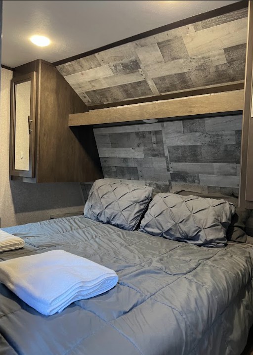 Comfortable RV rental bedroom featuring a gray bed, decorative pillows, and stylish wood-look interior walls.. Dutchmen Coleman Lantern 2020
