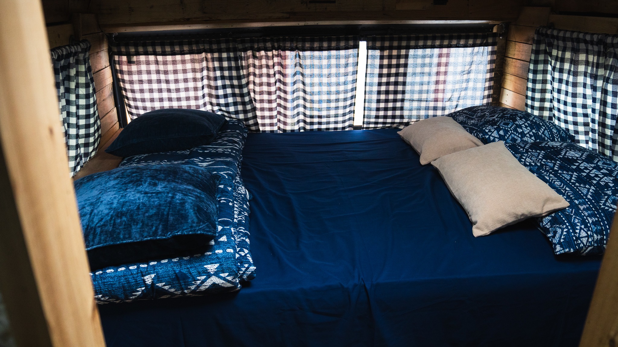 Cozy RV rental bed with dark blue sheets, patterned duvets, and checkered curtains creating a comfortable sleeping nook.. Freightliner FS 65 2007