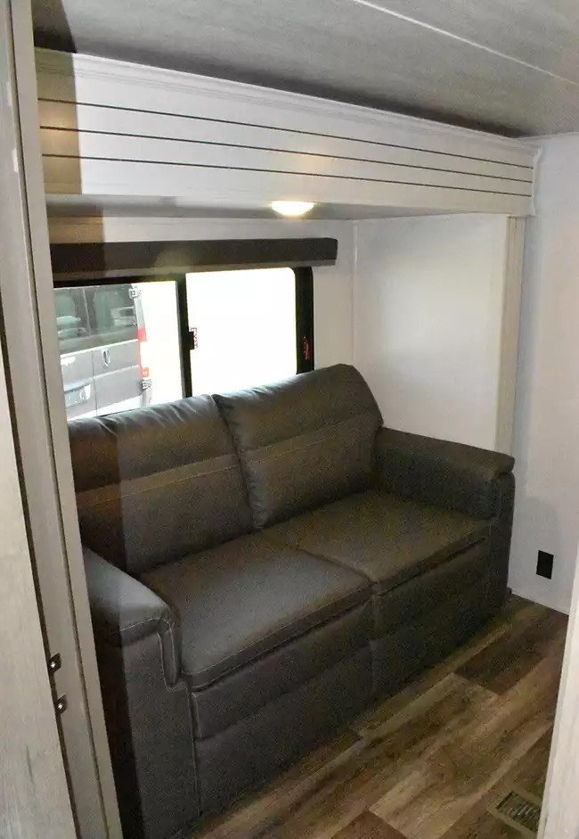 Inside this RV rental, a comfy gray sofa and window view create a cozy, practical living space with wood flooring.. Keystone Cougar 2021