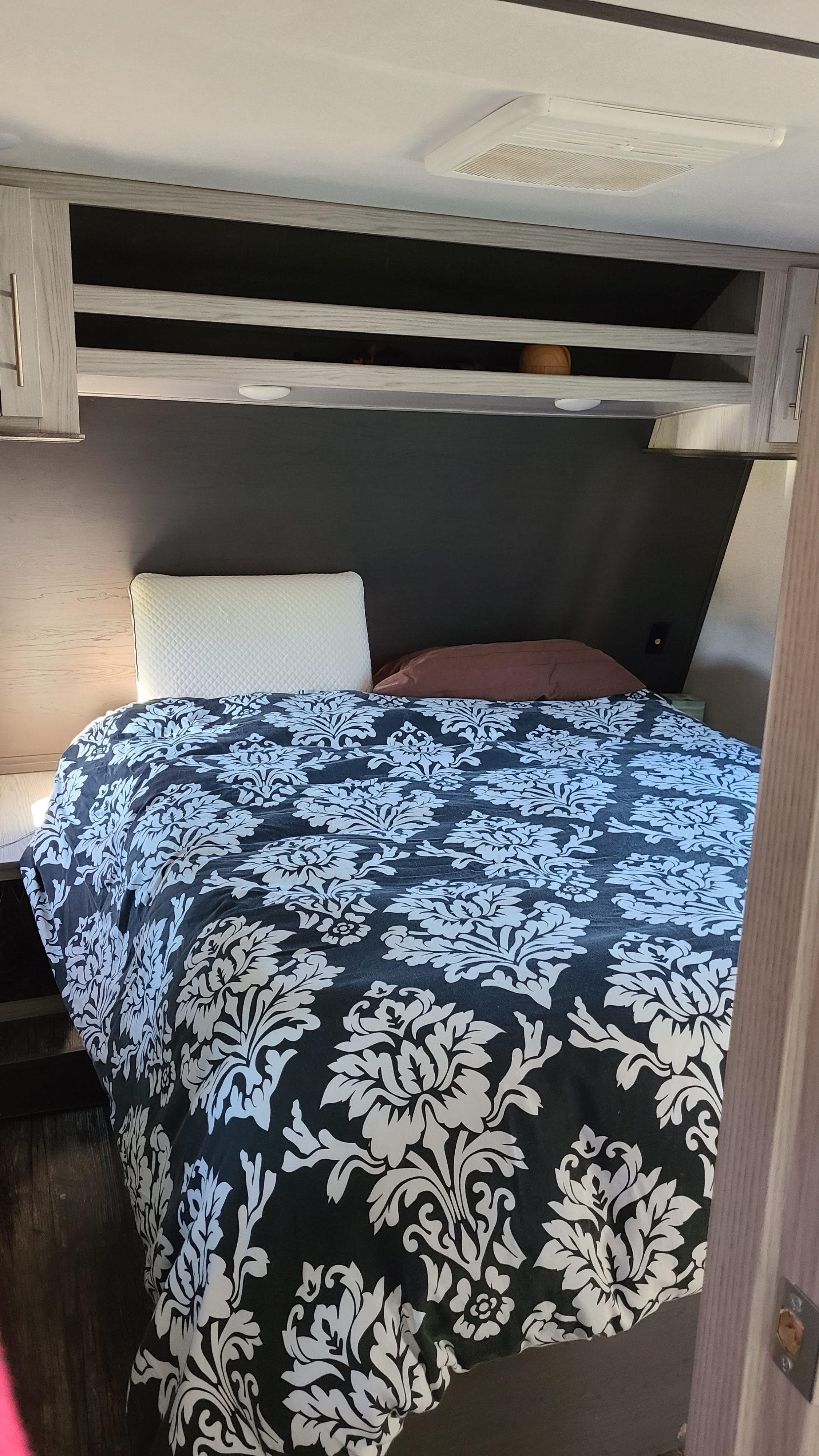 Cozy RV rental bedroom features a bed with a black and white damask duvet, pillows, and overhead storage.. Keystone Impact 2021