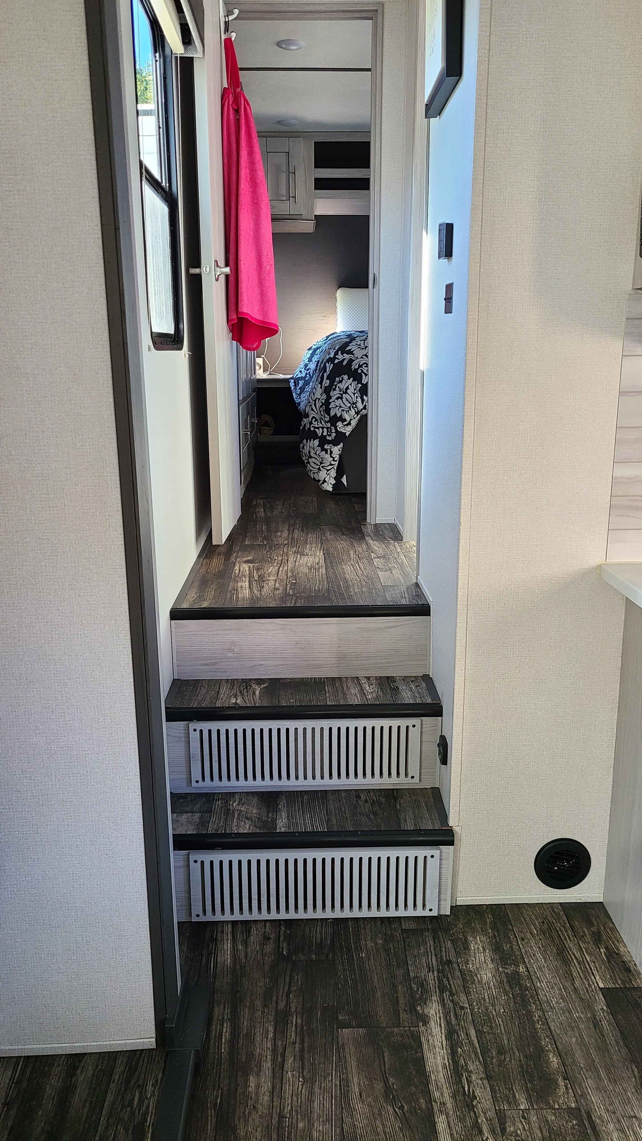 Inside an RV rental showing steps to a hallway leading to the bedroom. Notice the dark wood floor and light walls.. Keystone Impact 2021