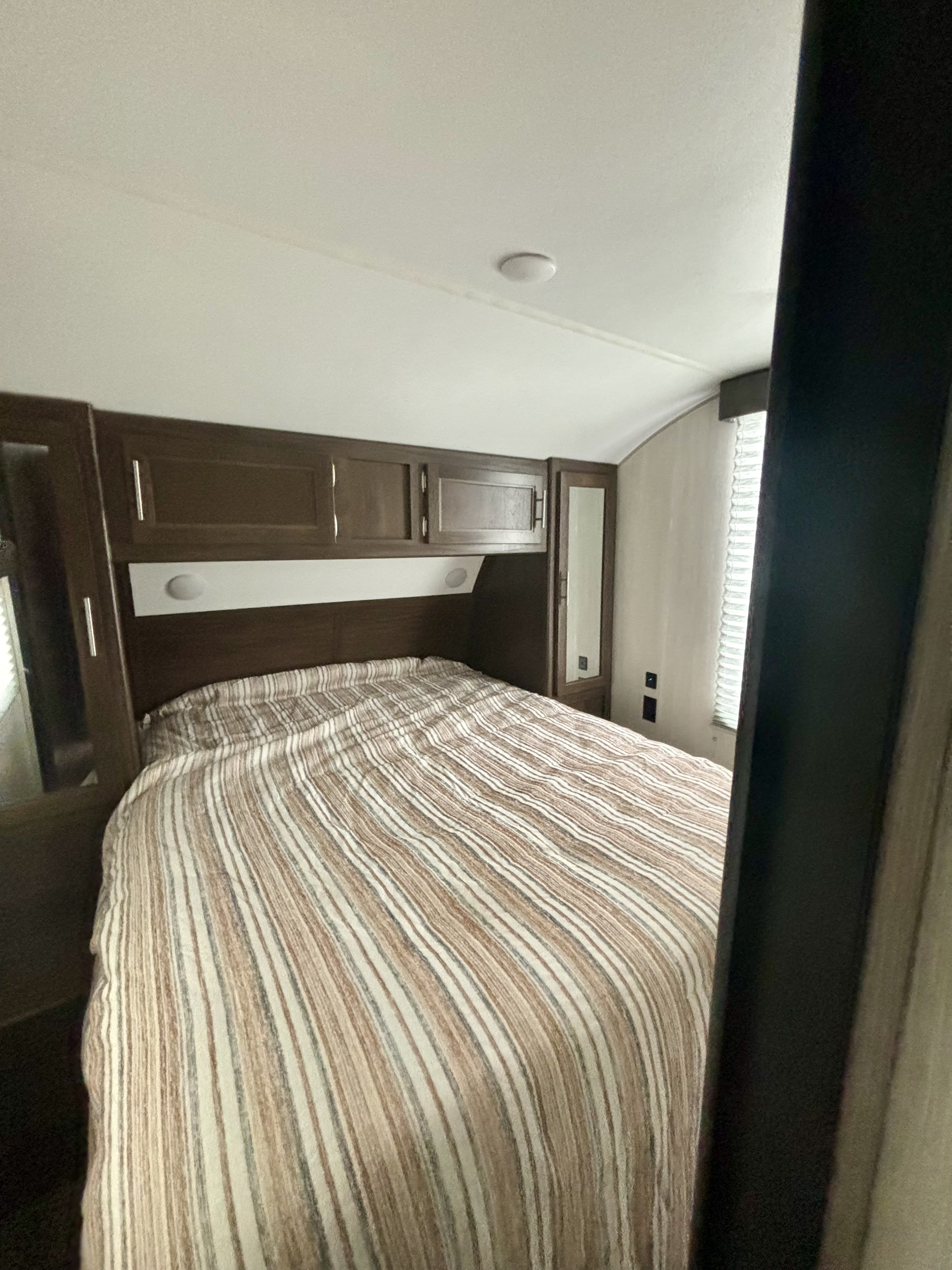 Cozy RV rental bedroom featuring a striped bedspread, functional overhead cabinets, and window blinds.. Forest River Cherokee 2019