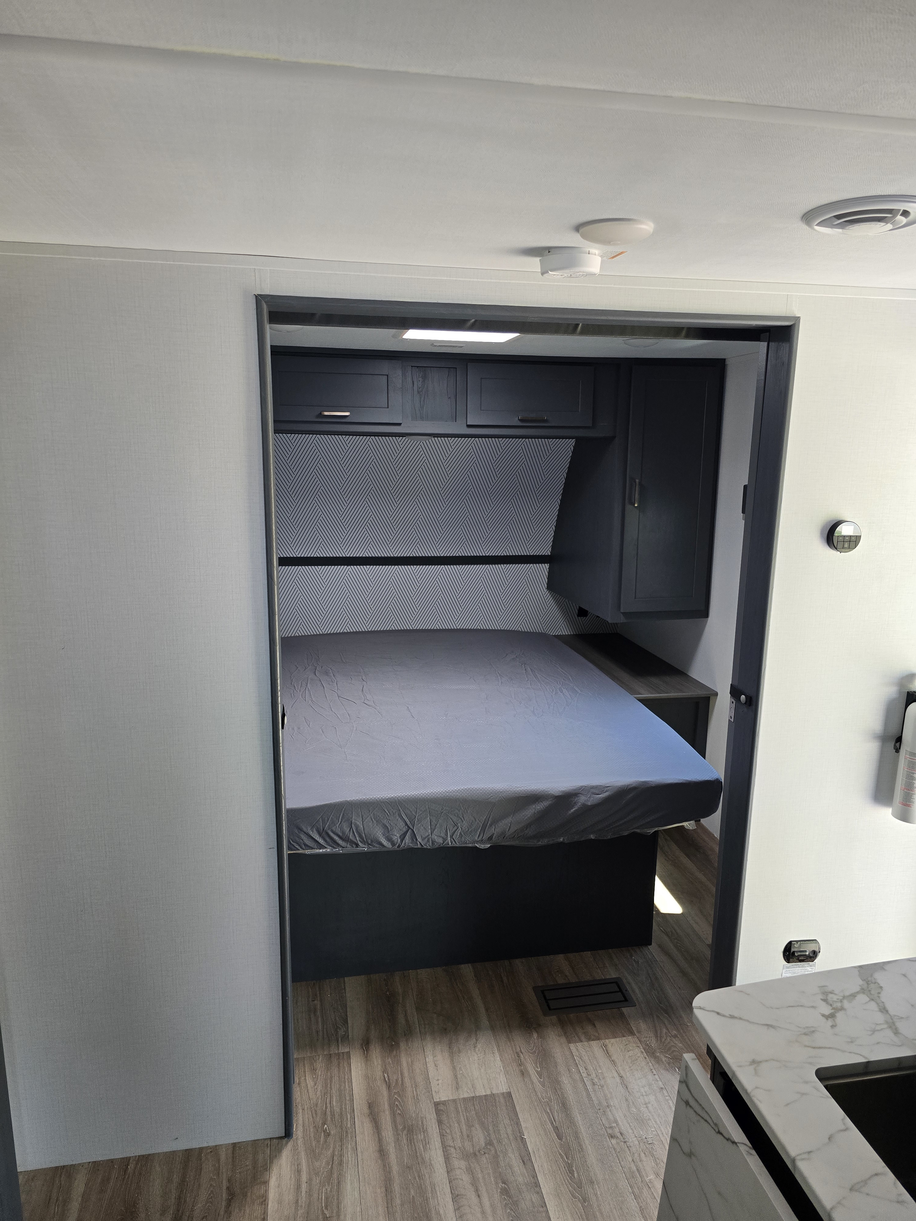 Modern RV rental interior: a compact bedroom with dark grey cabinets, patterned accent wall, and wood-look flooring.. Keystone RV Bullet Crossfire 2024