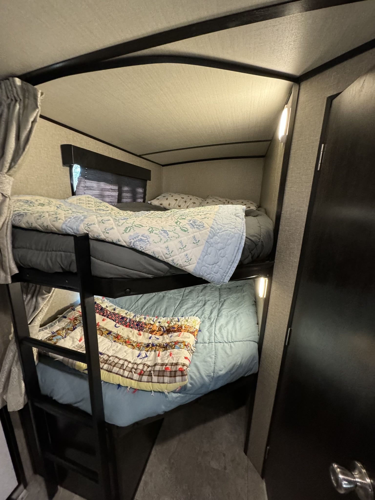 Cozy RV rental bunk beds feature patterned quilts and reading lights, offering comfortable sleeping for travel.. Grand Design Imagine 2019