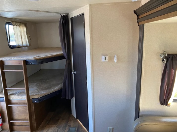RV rental interior: bunk beds with ladder & window, privacy curtain, door, and thermostat on wall.. Forest River Wildwood 2018