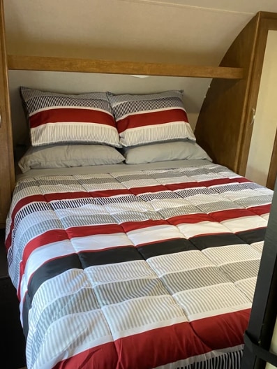 Cozy RV rental bedroom: a bed with red, white, & gray striped bedding and wood storage above.. Forest River Wildwood 2018