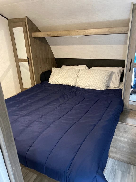 This RV rental bedroom offers a comfortable bed with blue bedding, white pillows, and built-in storage on both sides.. Heartland RVs Pioneer 2021