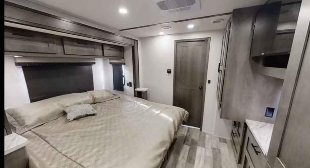 Comfortable RV rental bedroom featuring a large bed, overhead cabinets, and wood-look flooring.. FR3 FR3 Motorhome 2023