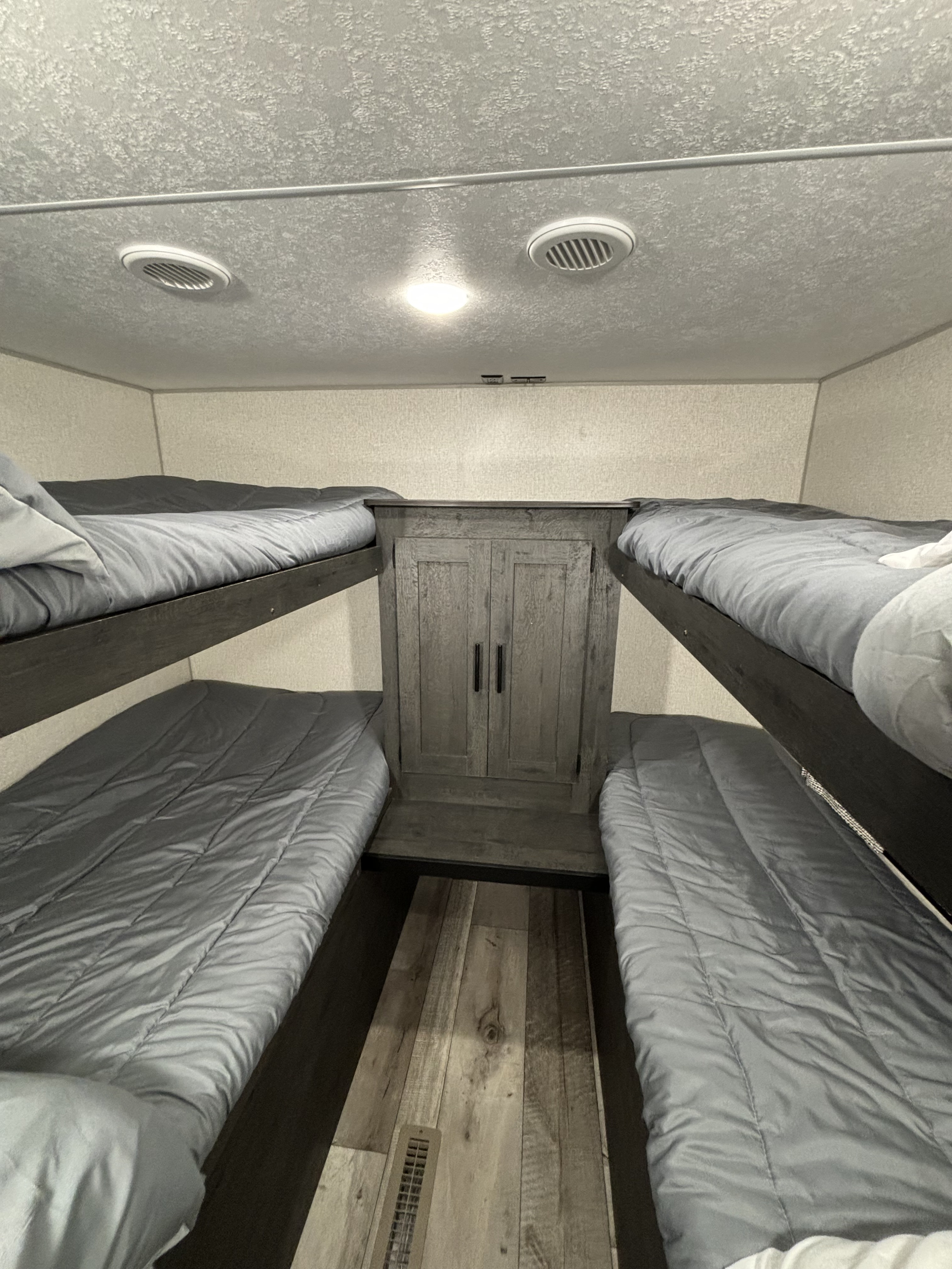 Compact RV rental bunk room showing four beds with grey bedding, a central cabinet, and wood-look floor.. K-Z Manufacturing Sportsmen 2022
