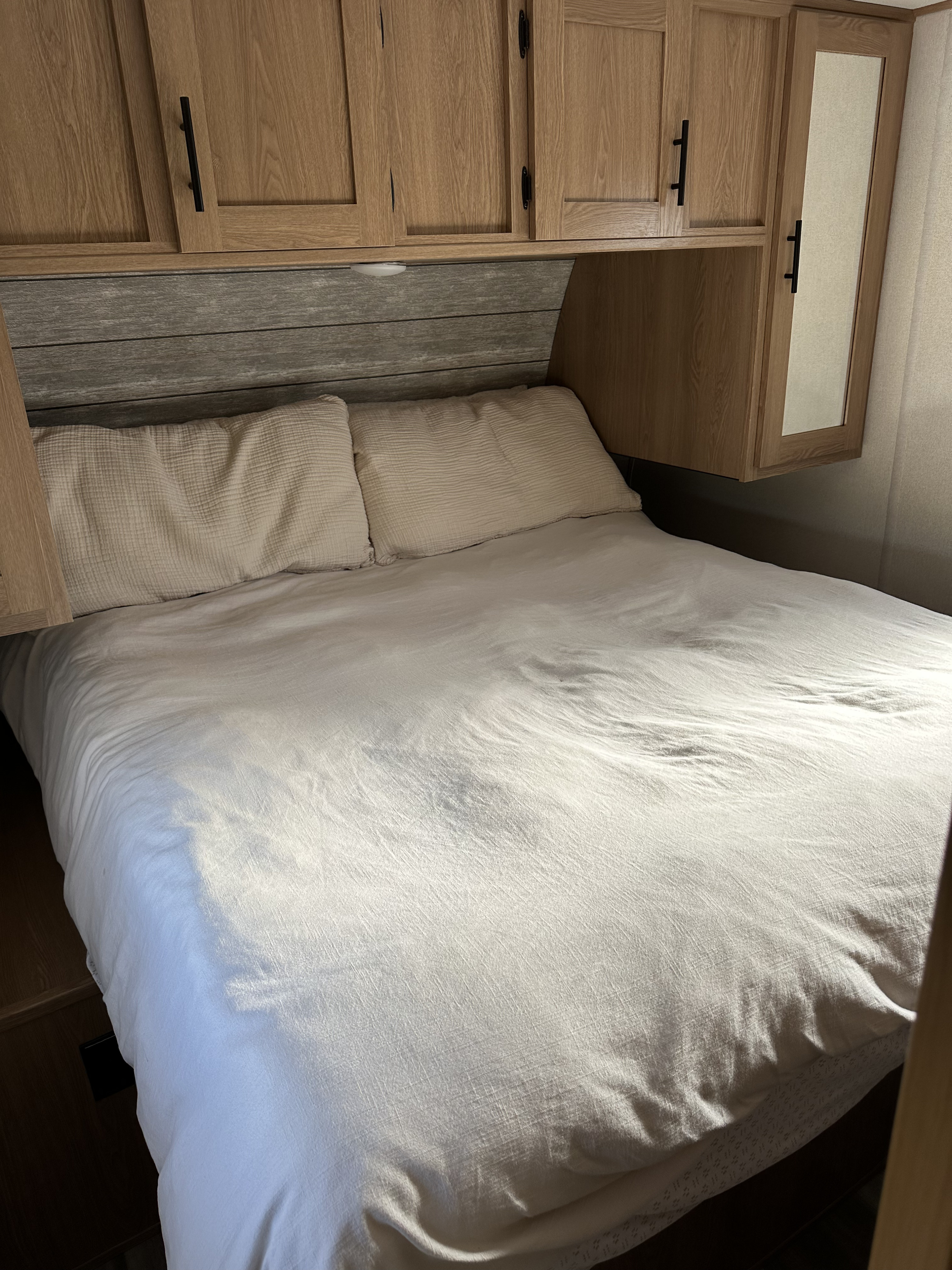Cozy RV rental bedroom features a comfy bed with crisp white bedding, sleek cabinets, and a wood-paneled headboard.. Forest River Avenger 2023