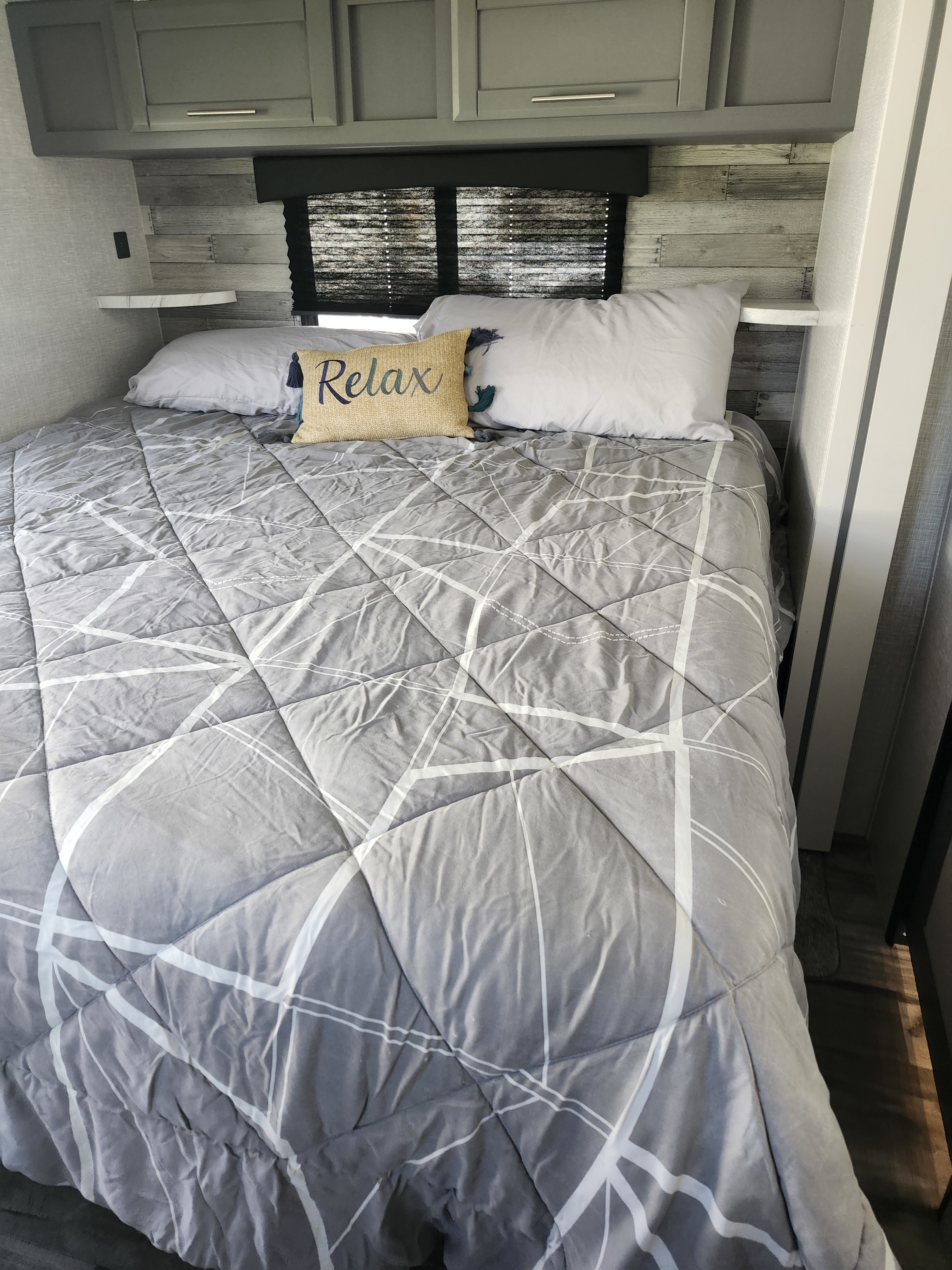 Cozy RV rental bedroom with a grey bed, 'Relax' pillow, and overhead cabinets. Perfect for your travels!. Crossroads RV Volante 2022