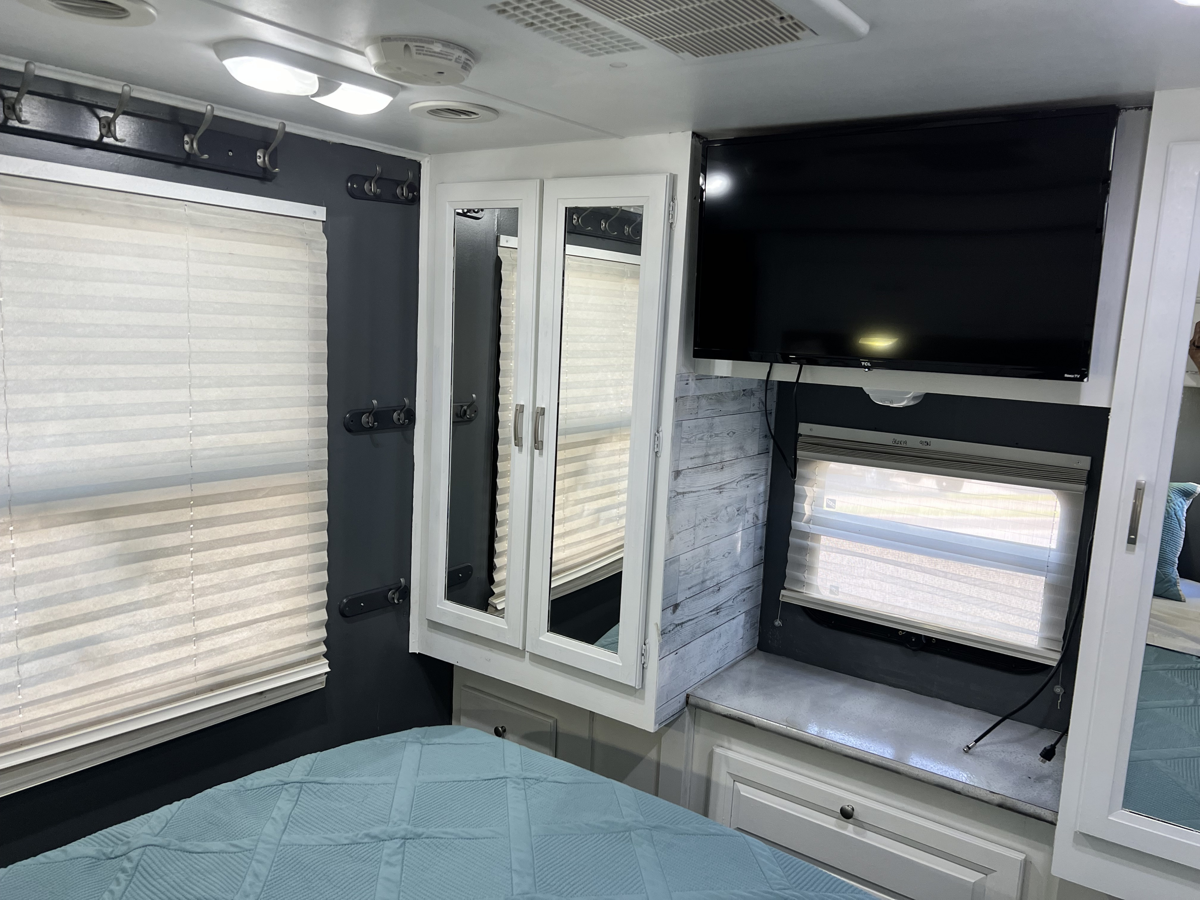 This RV rental bedroom features a blue quilted bed, mounted TV, mirrored cabinets, and privacy blinds on windows.. Forest River Georgetown 2014