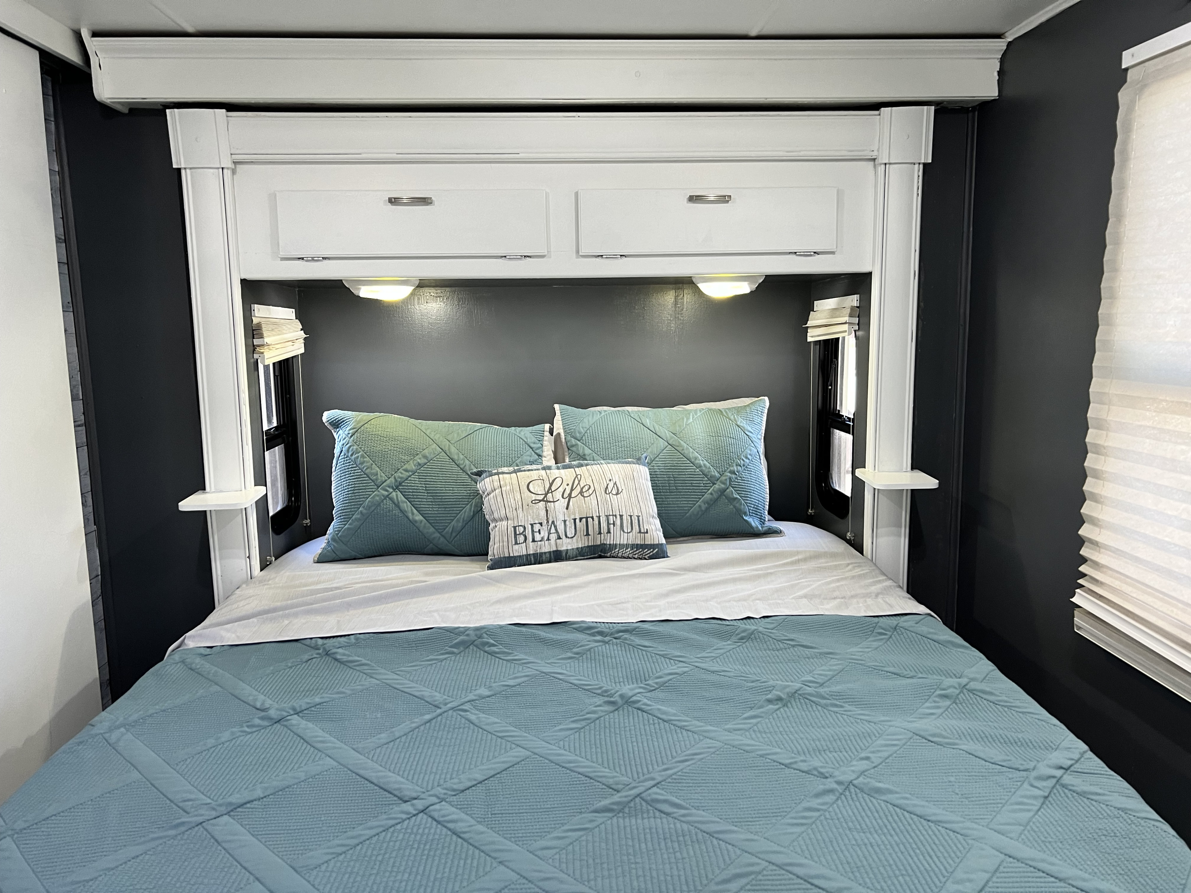 Cozy RV rental bedroom with a comfy bed, blue bedding, overhead storage, reading lights, and a 'Life is Beautiful' pillow.. Forest River Georgetown 2014