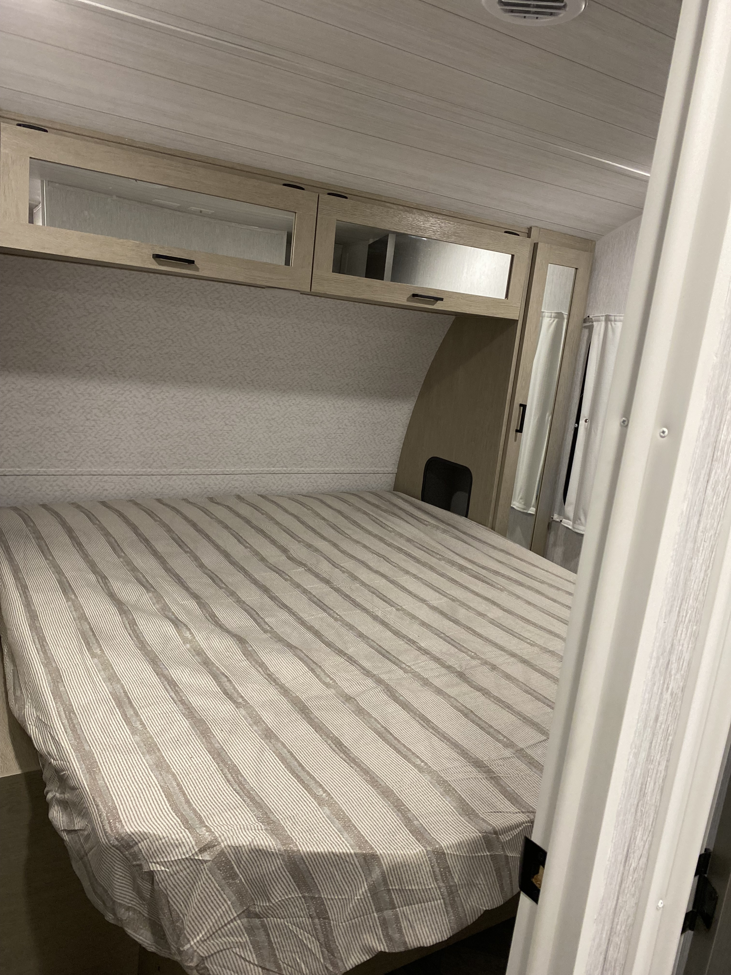 Cozy RV rental bedroom with striped bedding, overhead cabinets, and a mirrored closet, offering comfortable travel accommodation.. Forest River Salem 2024