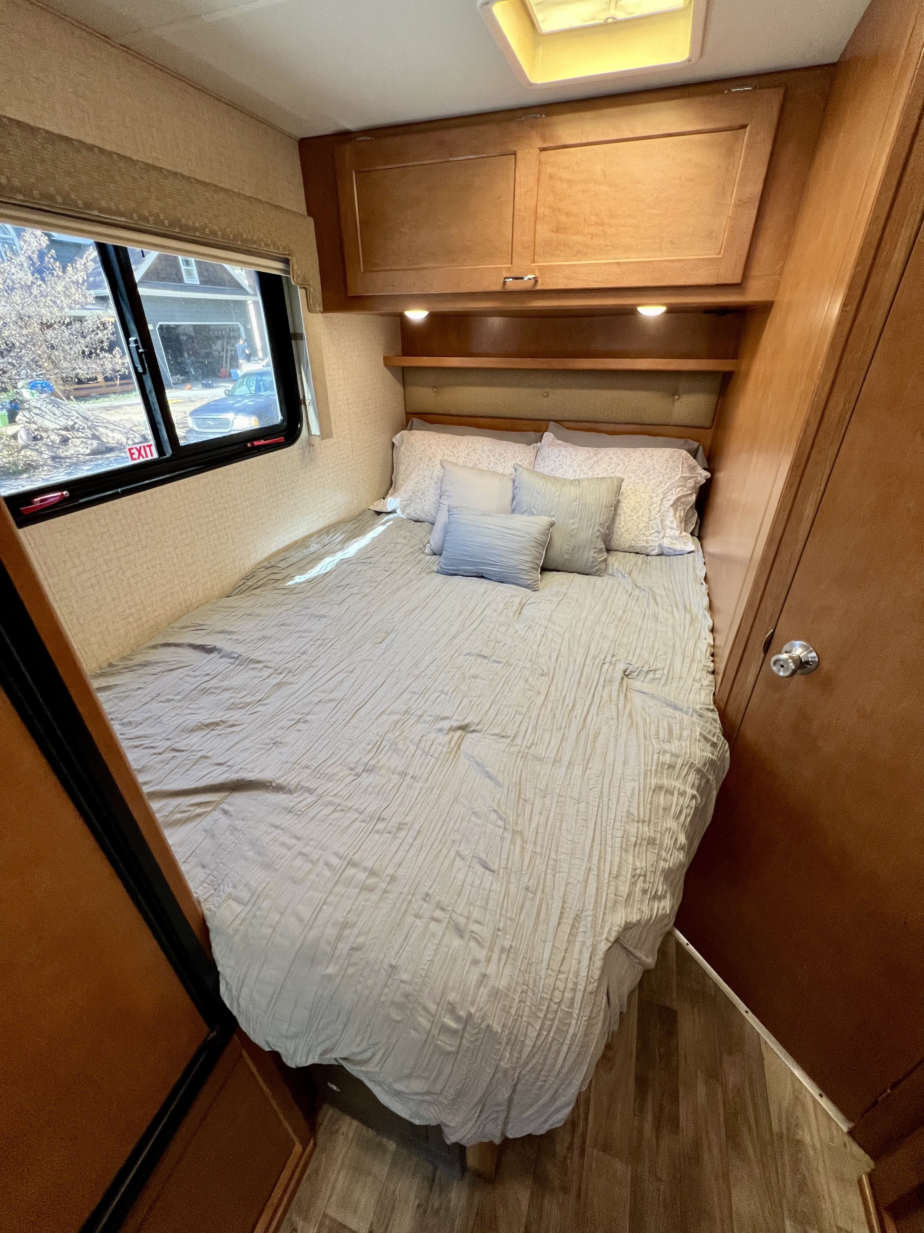 Explore compact living in this RV rental bedroom, featuring a comfy bed, overhead storage, and a scenic window view.. Winnebago Minnie Winnie 2017