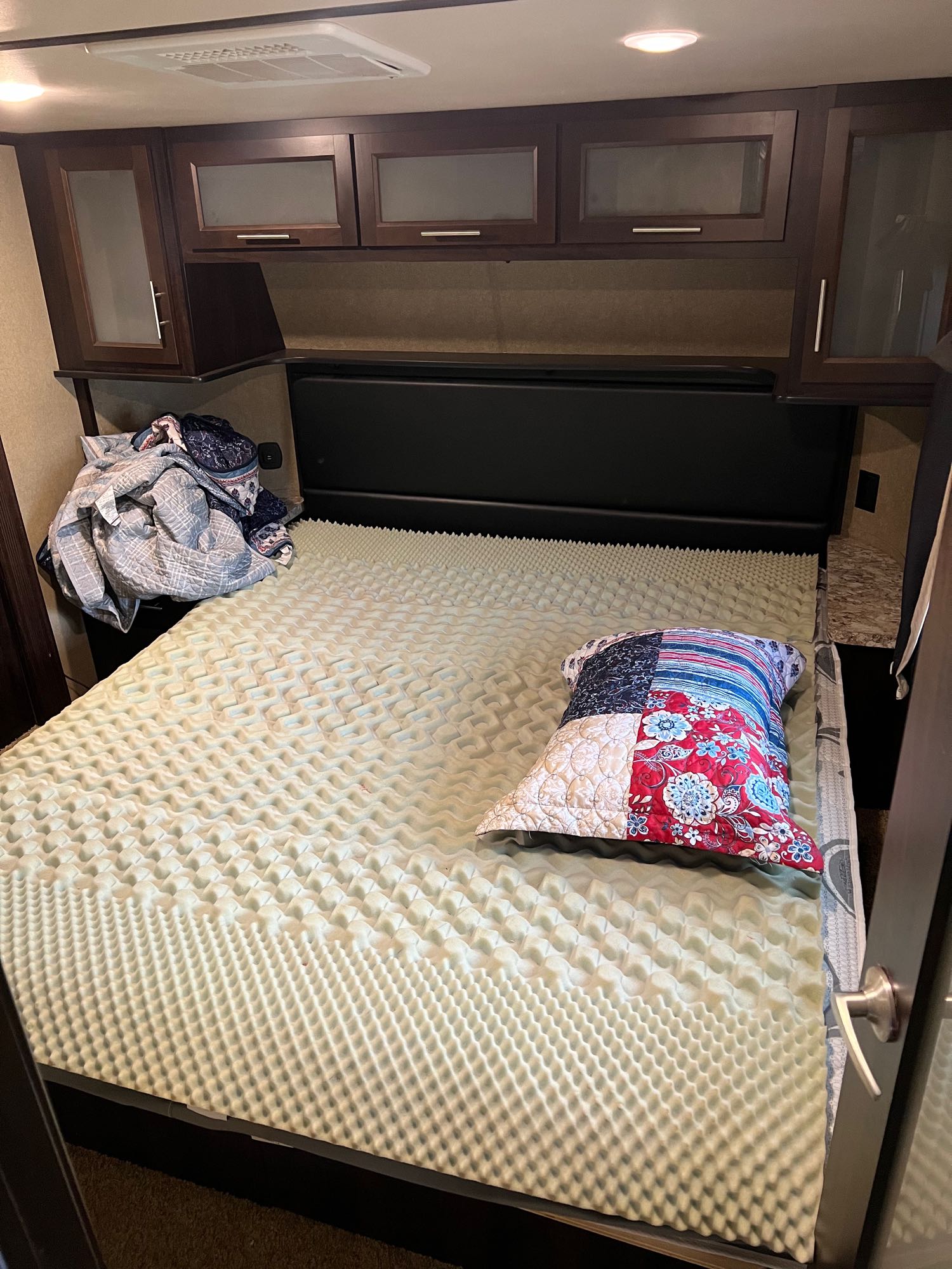 Cozy RV rental bedroom featuring a bed with an egg crate topper, colorful pillow, and overhead storage cabinets.. Forest River Xlr Thunrderbolt 2017