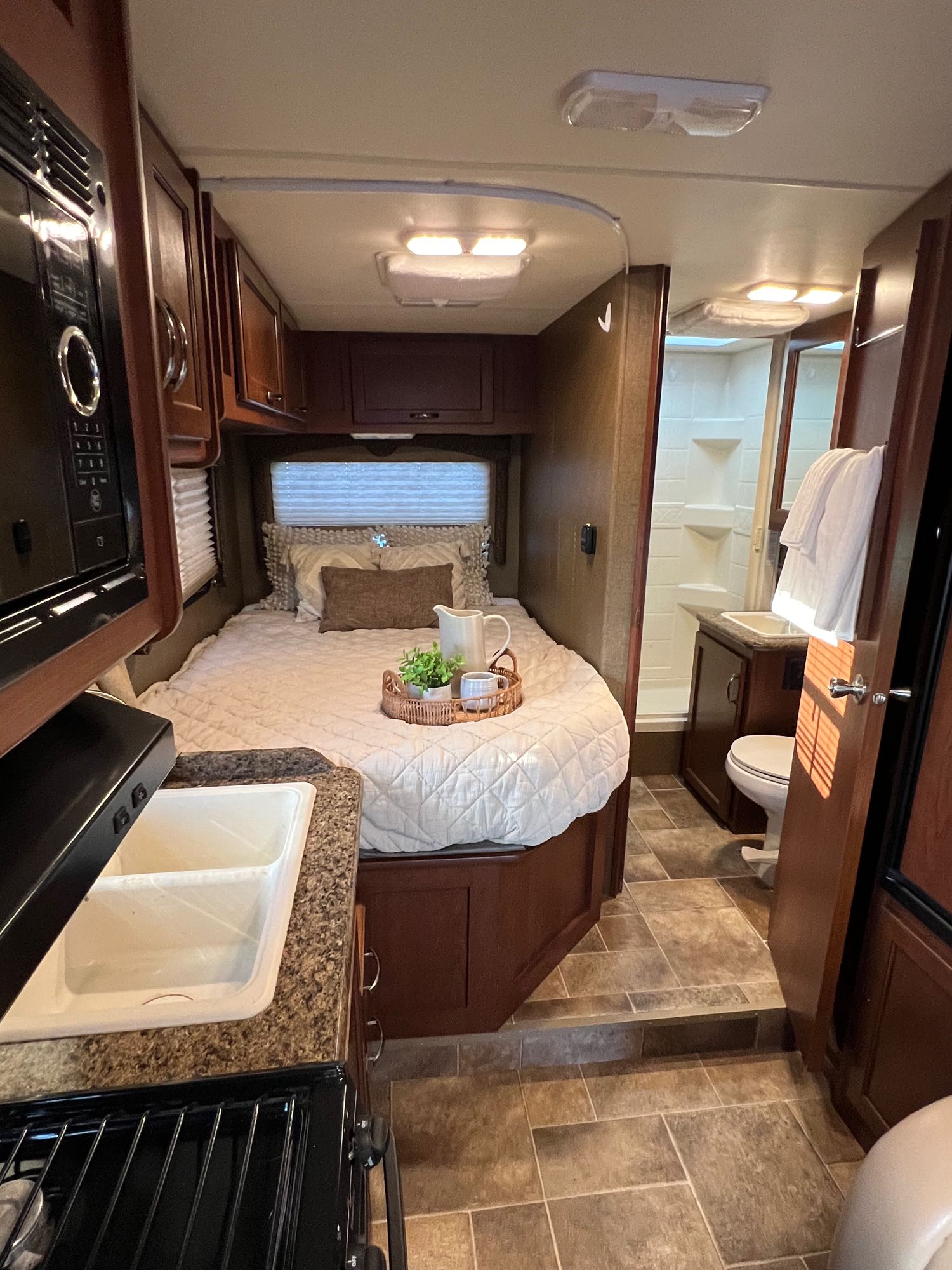 This RV rental interior showcases a compact kitchen, a cozy bedroom with a decorative tray, and a full bathroom entrance.. Thor Freedom Elite 2015