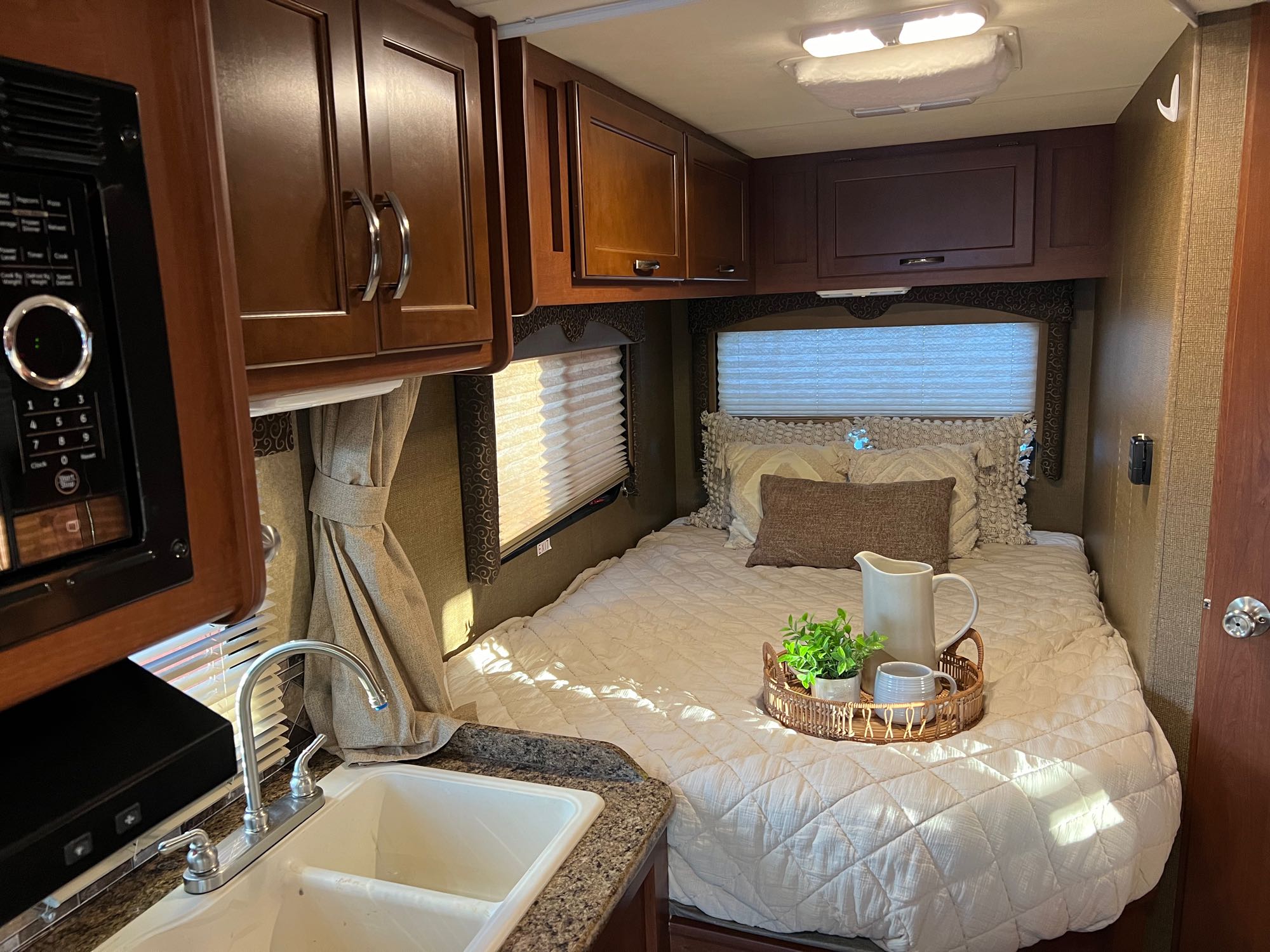 Cozy RV rental interior featuring a compact kitchen with sink and microwave, plus a comfortable bed area.. Thor Freedom Elite 2015