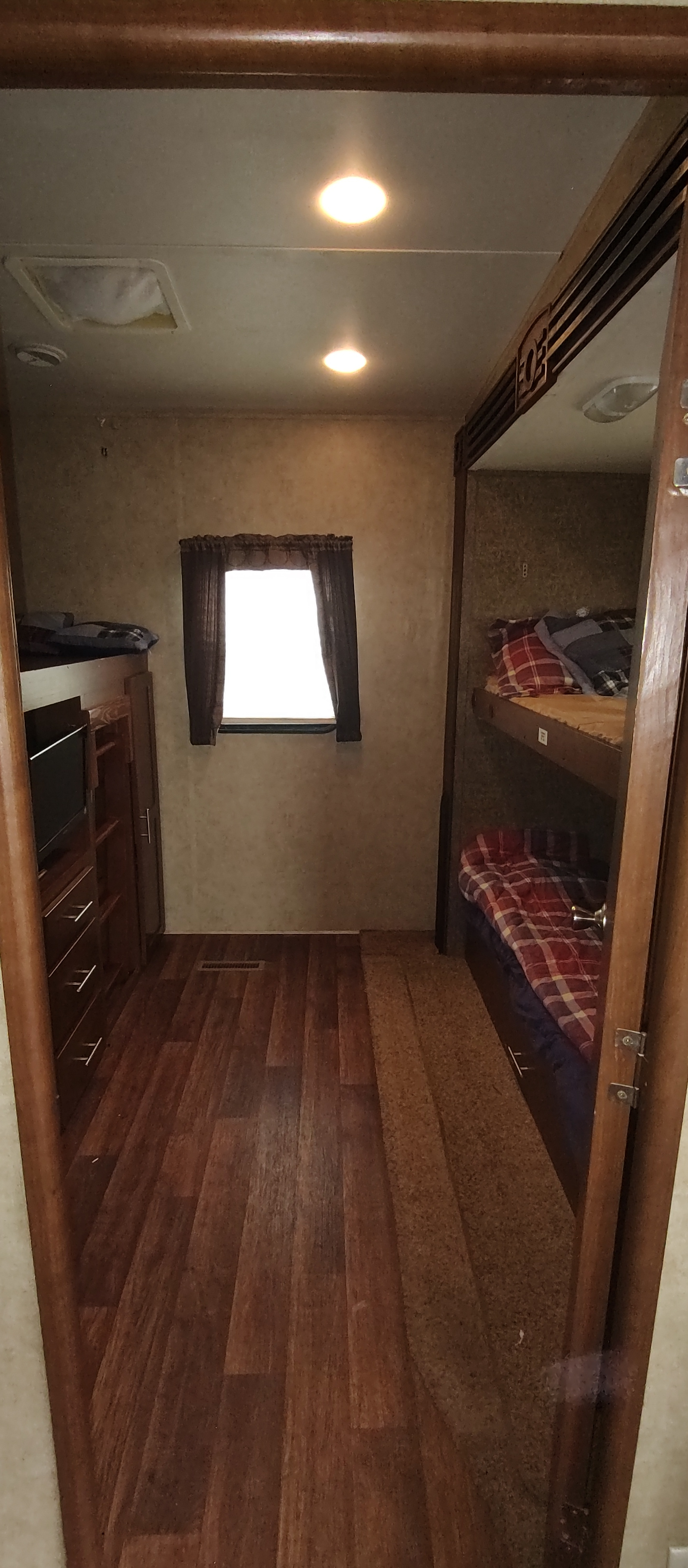 RV rental bunkhouse: An interior view showing a hallway with wood floor, central window, and bunk beds with storage & TV.. Dutchmen Komfort 3530fbh 2012