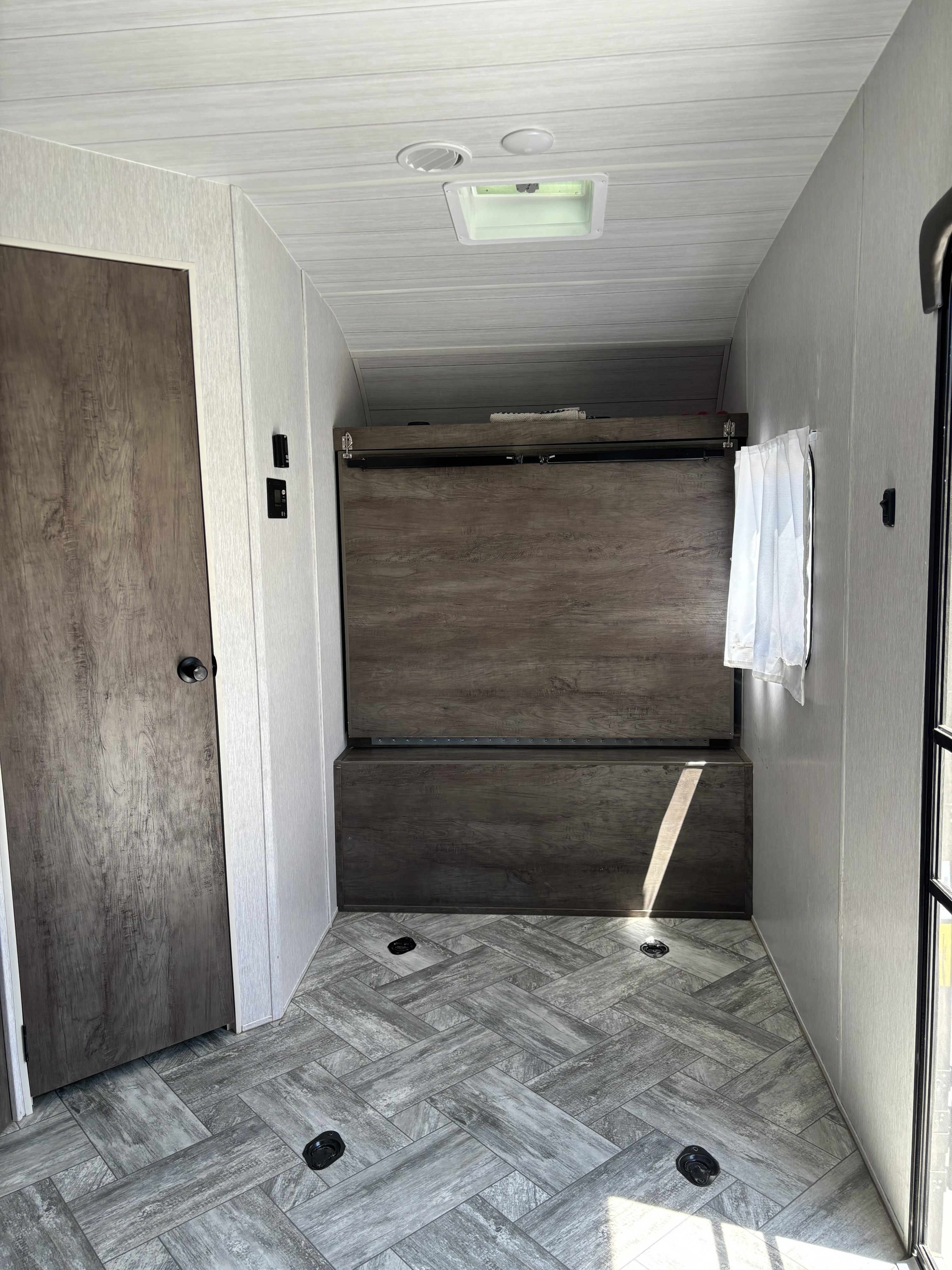 RV rental interior featuring a versatile fold-down bunk bed, modern herringbone flooring, and light-toned walls.. Forest River Stealth 2022