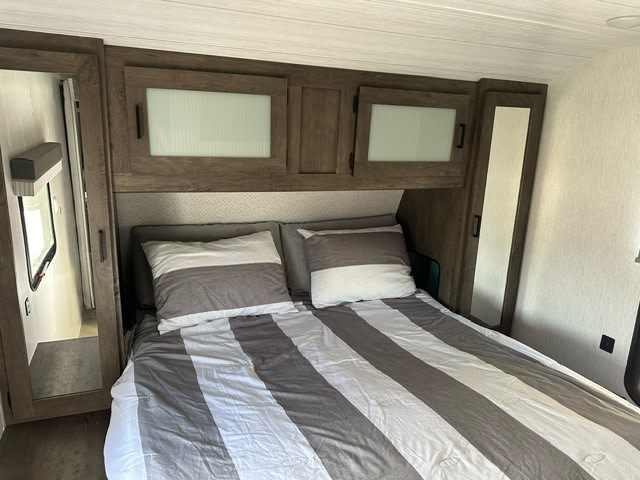 Cozy RV rental bedroom features striped bed, overhead cabinets, and mirrored wardrobes. Ideal compact space.. Forest River Salem 2022