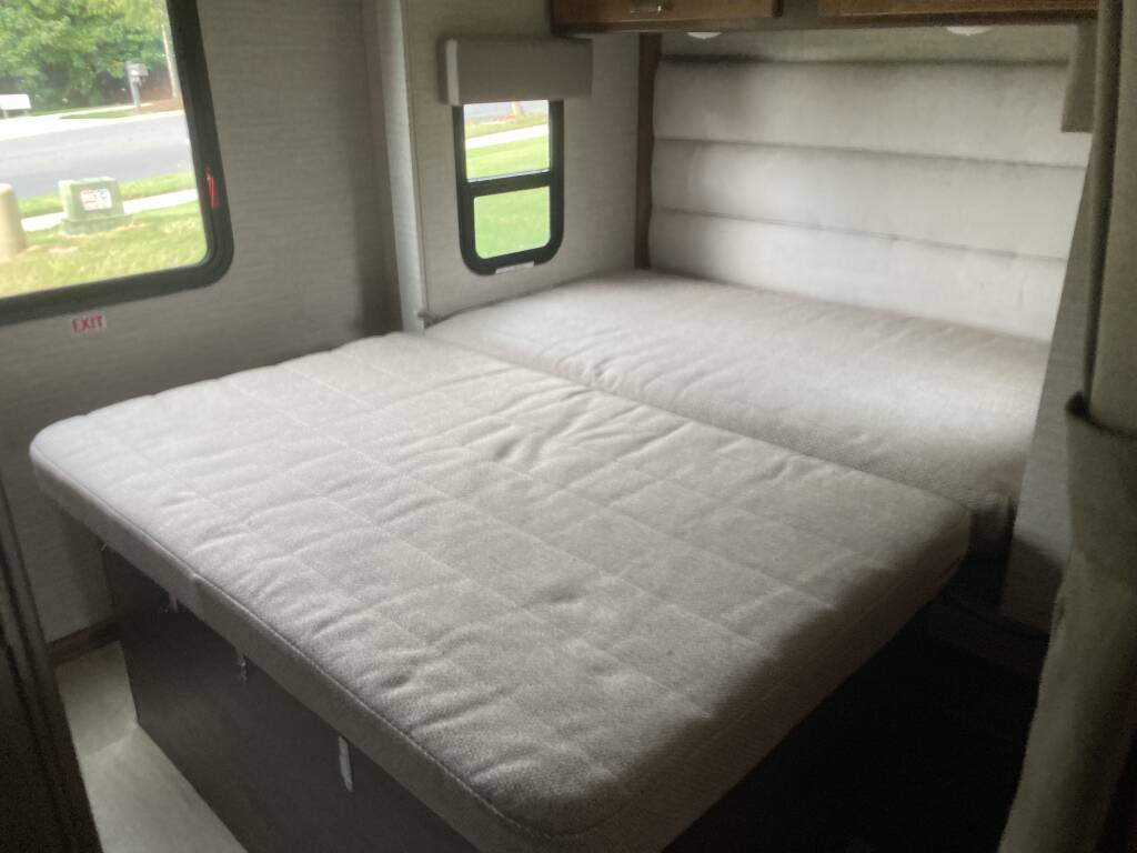 This RV rental interior features a cozy, light-colored pull-out bed setup with two mattress sections, padded walls, and windows.. Winnebago Minnie Winnie 2020