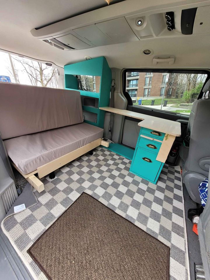 Inside this RV rental van conversion: a cozy bed, teal storage, and pull-out desk, perfect for mobile travel.. dodge grand caravan 2008