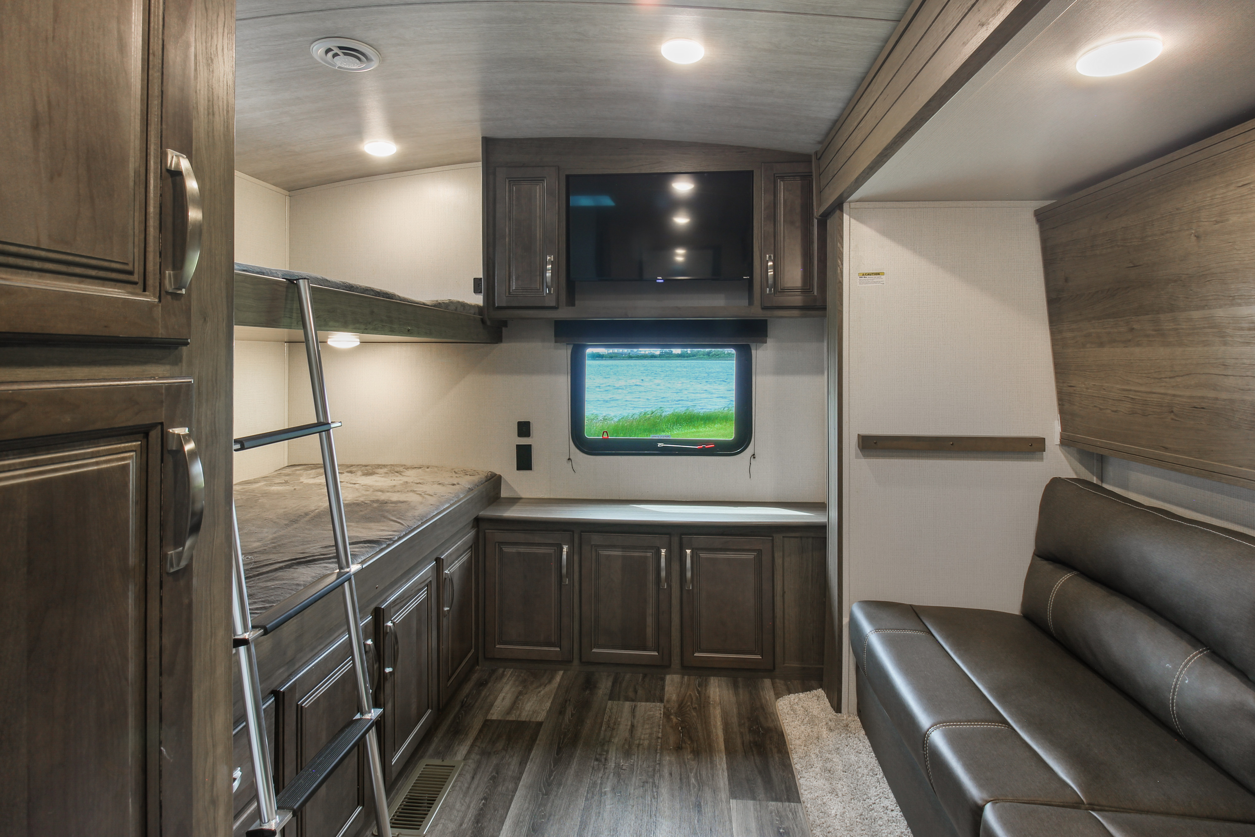 Experience a cozy RV rental! This interior features bunk beds, a TV, storage cabinets, a sofa, and a scenic window view.. Keystone RV Cougar 2021