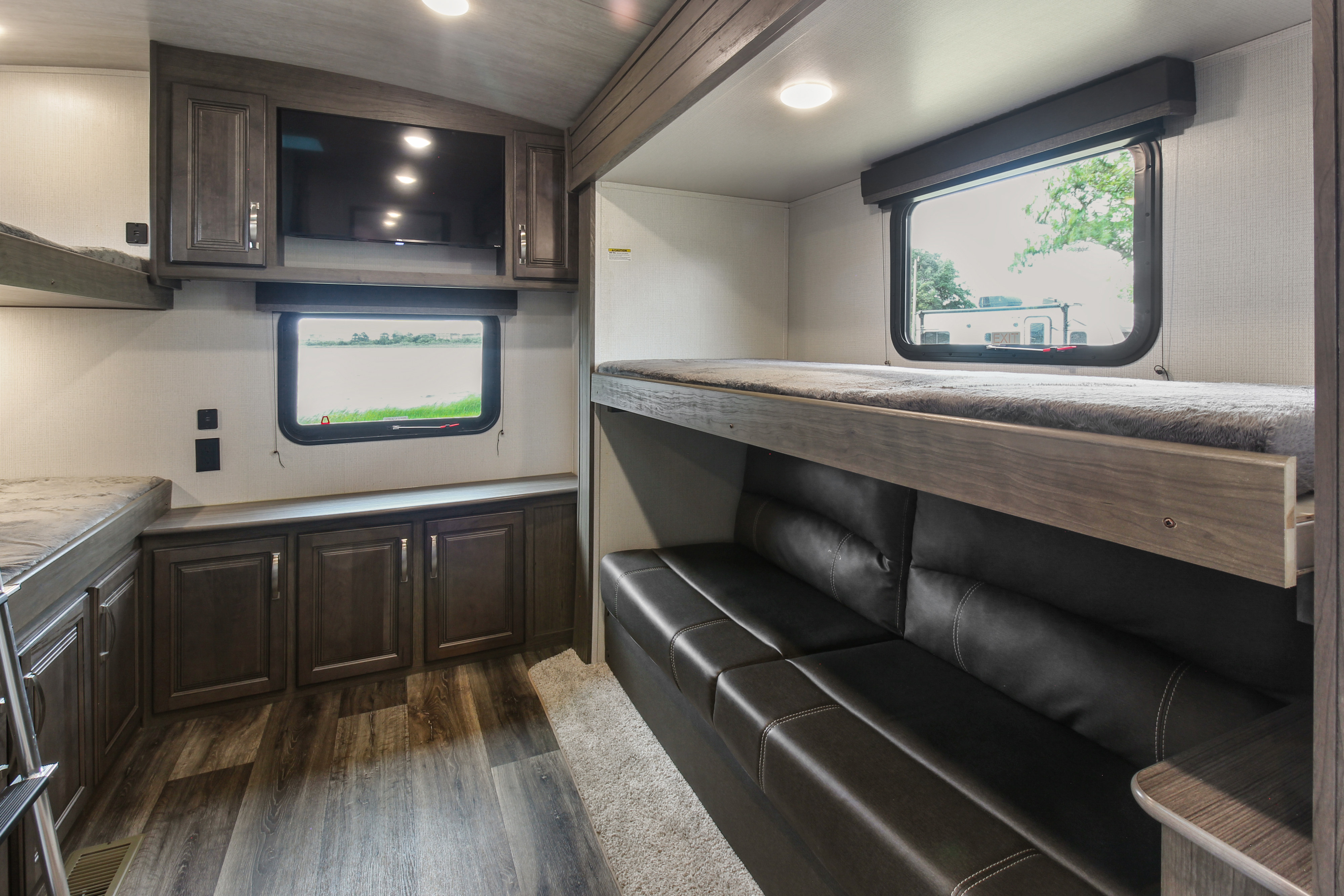 Modern **rv rental** bunkhouse interior featuring dual bunk beds, a leather sofa, and TV for family comfort.. Keystone RV Cougar 2021