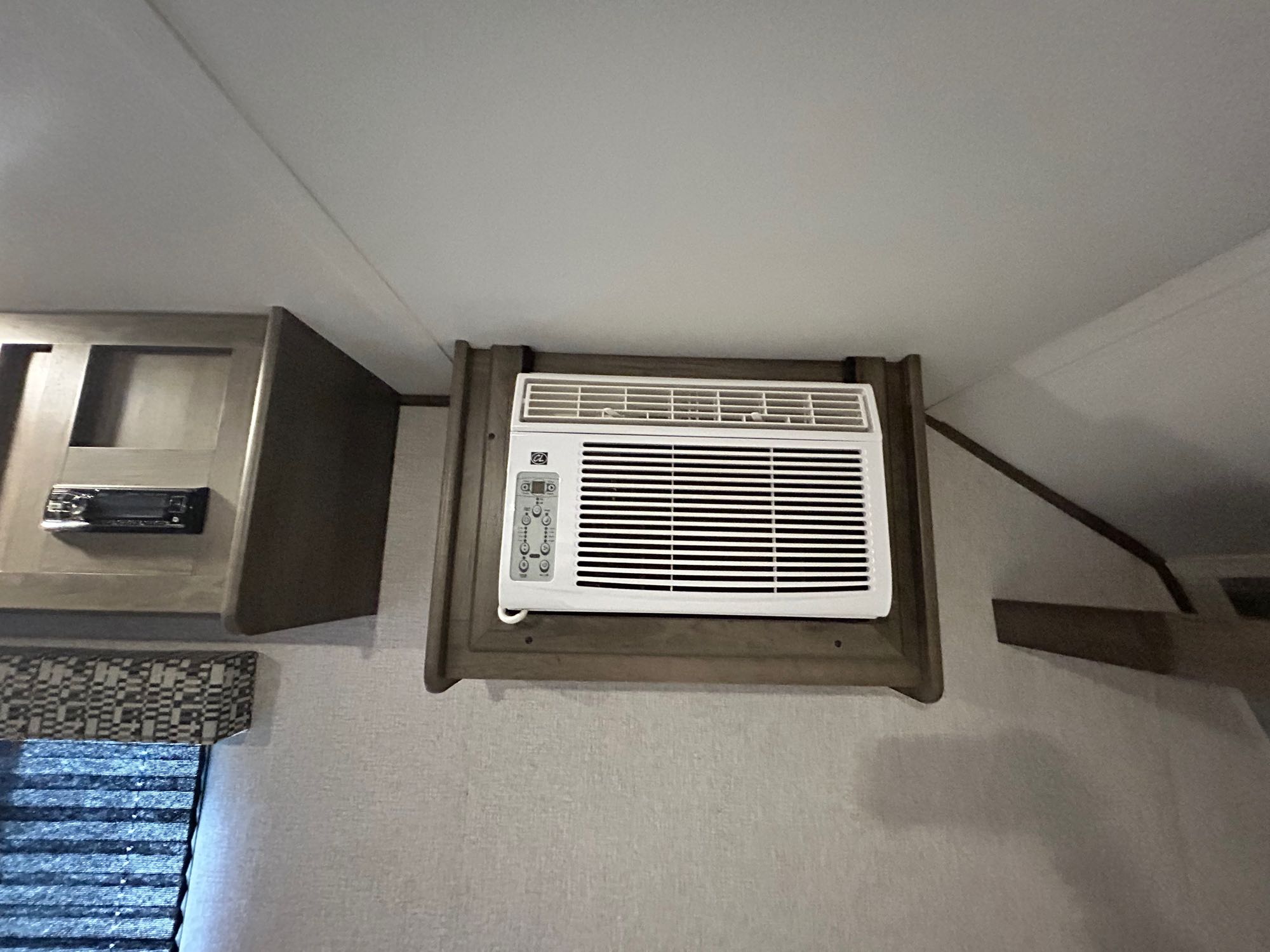 Interior of an RV rental showing a compact AC unit mounted in wooden trim, alongside cabinetry and a window with blinds.. Aspen Trail LE 2021