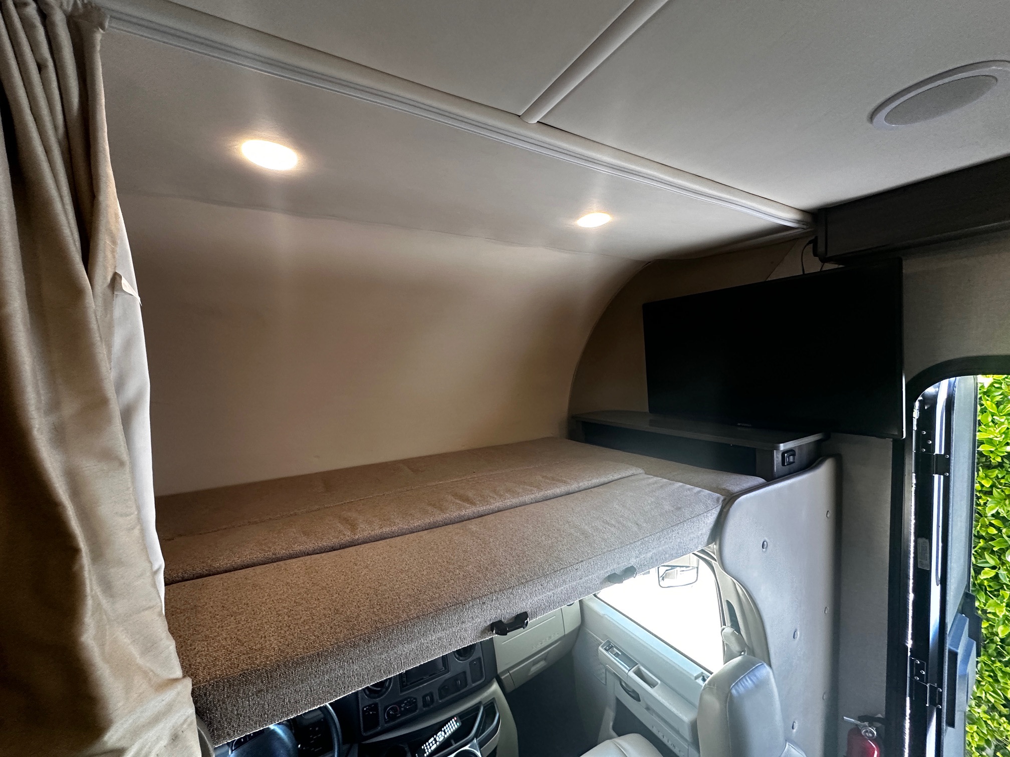 Inside an RV rental: a spacious cab-over bunk bed with a mounted TV, ample head room, and bright interior lighting.. Holiday Rambler Augusta 2019