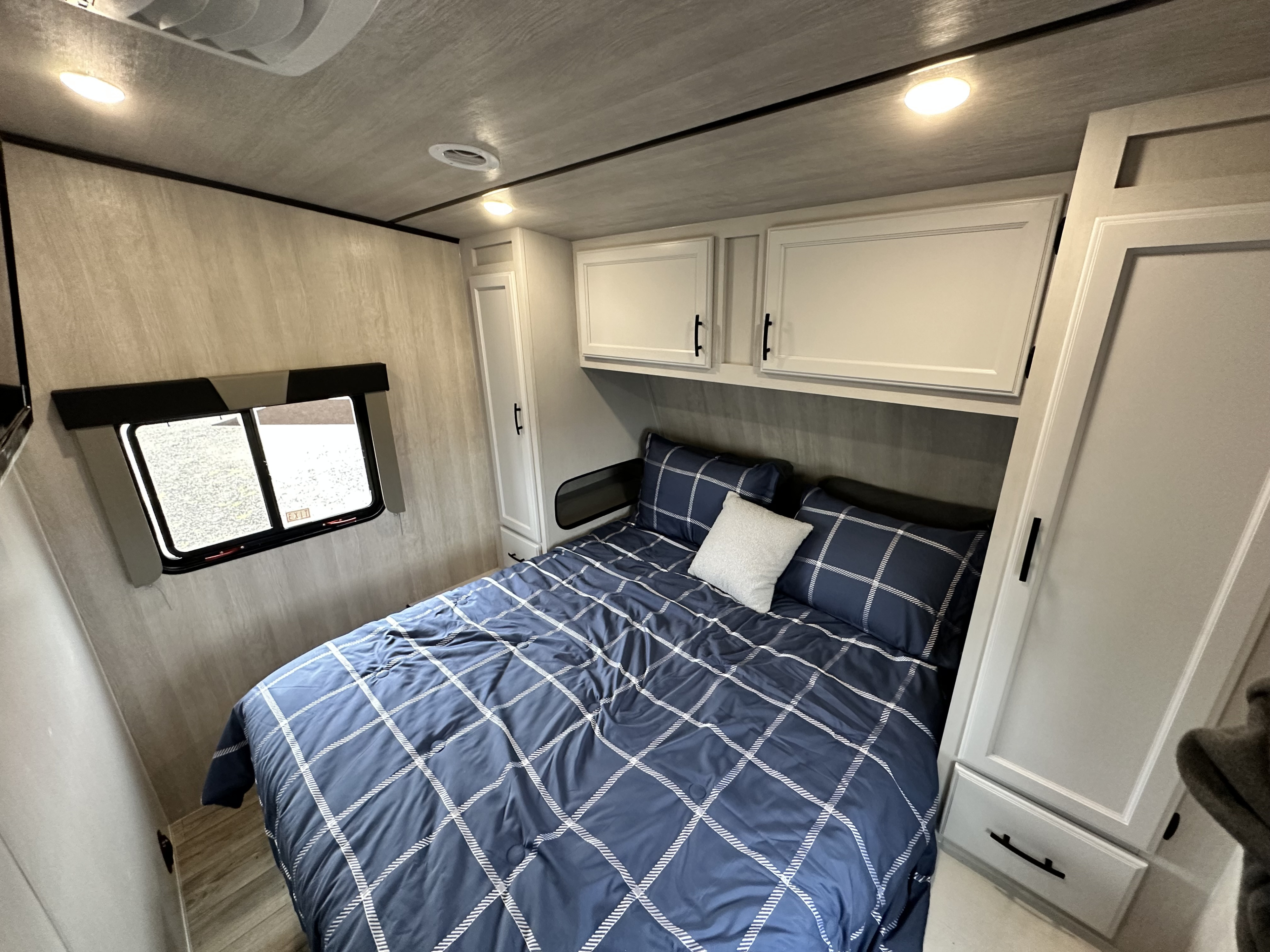 Explore this modern RV rental bedroom featuring a comfortable bed with blue plaid bedding, window, and compact storage.. Genesis Supreme Rv Genesis Supreme 2024