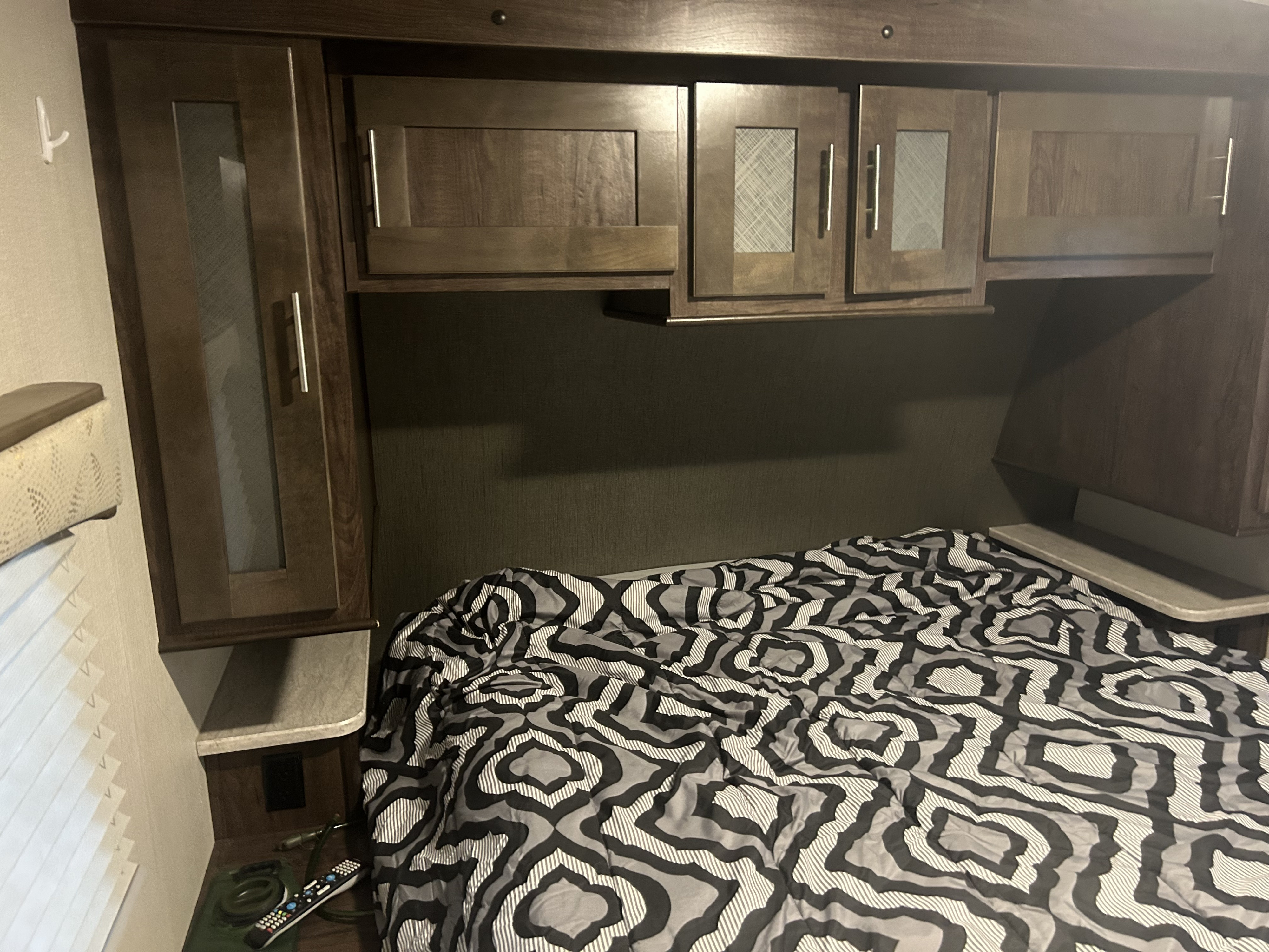 Cozy RV rental bedroom featuring a patterned comforter, dark wood cabinets, and convenient bedside storage.. Cruiser RV Embrace Ultra Lite 2019