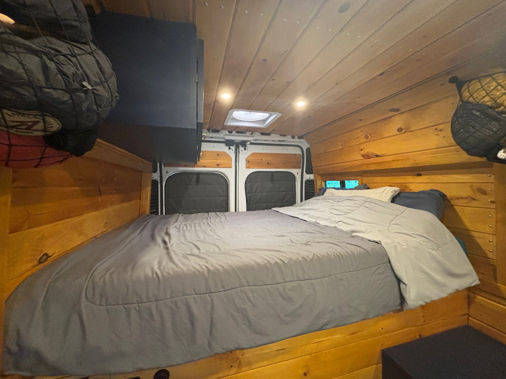Experience this cozy rv rental! Van interior features a comfortable bed, wooden walls, ceiling lights, and overhead storage.. ram promaster 2020