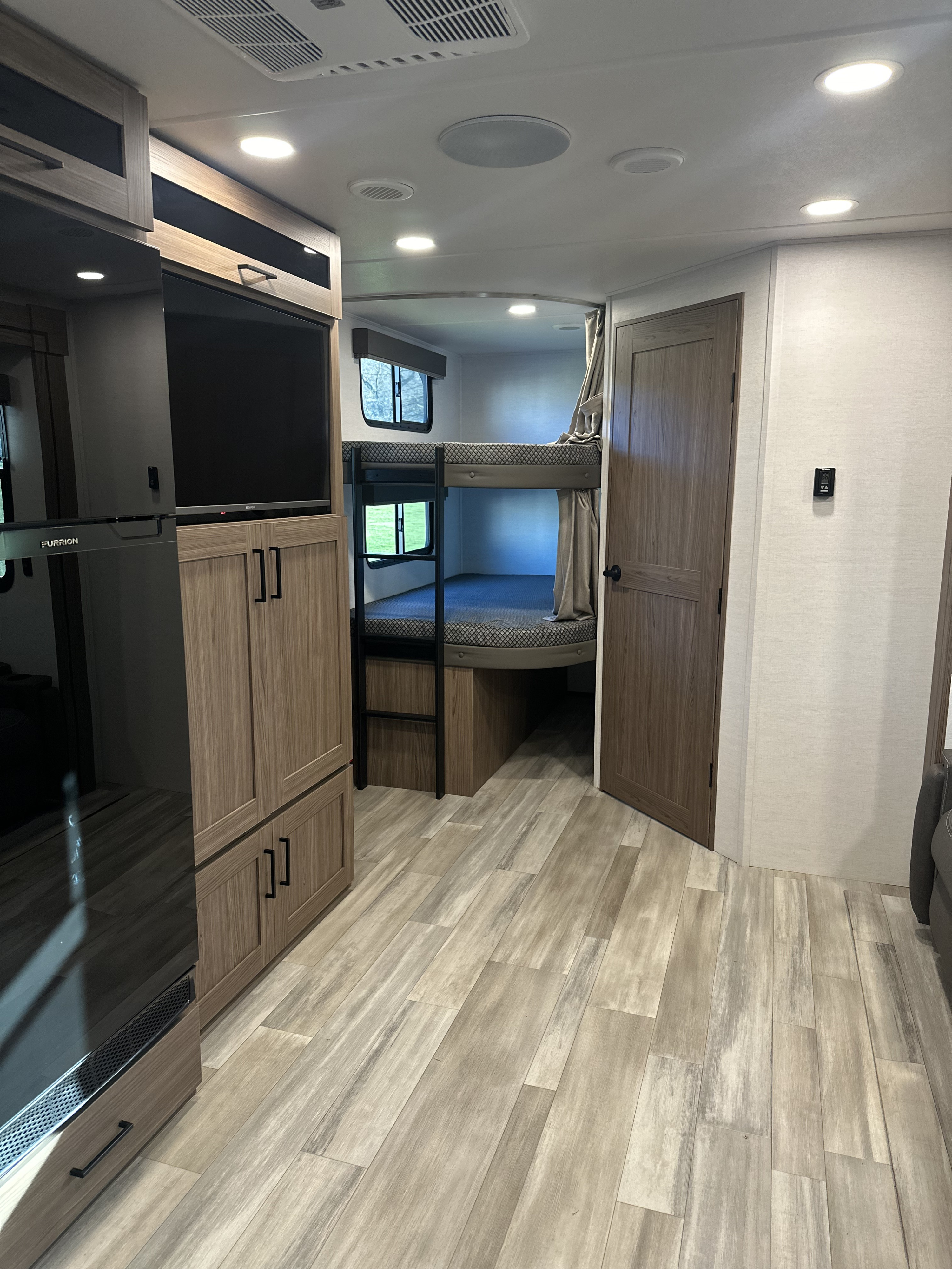 Tour a modern RV rental interior with bunk beds, fridge, TV, and wood-look flooring. Comfort for family trips.. Alliance Delta 281BH 2024